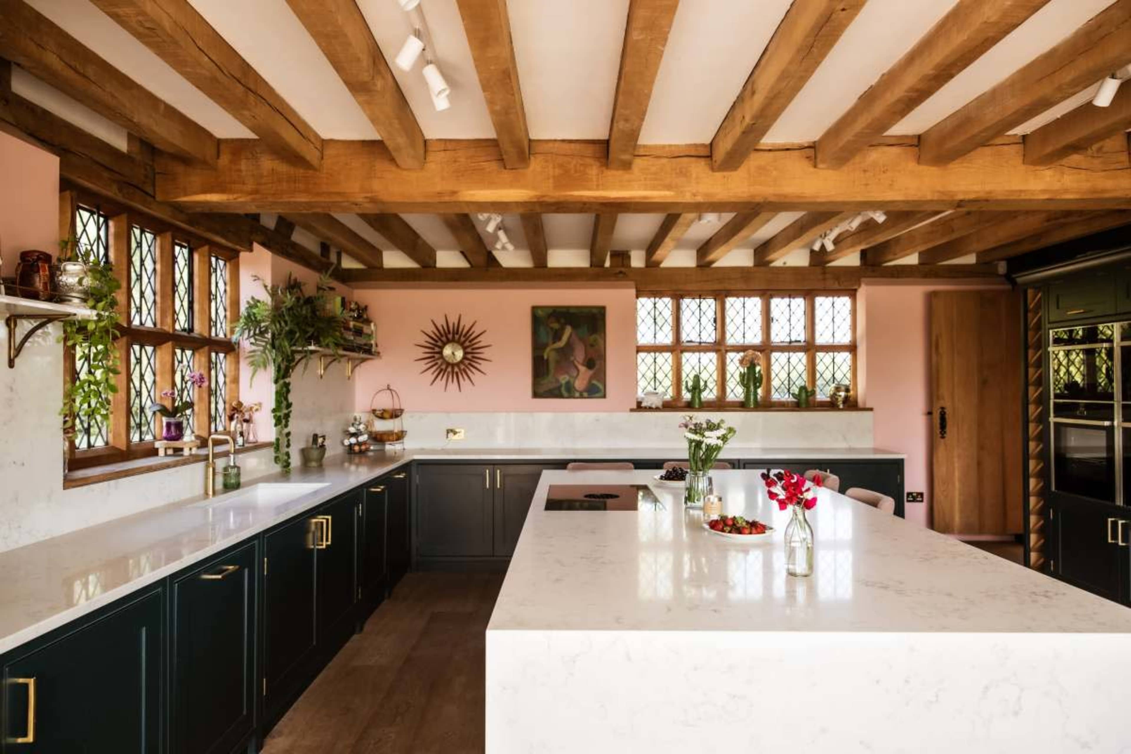 A modern kitchen features dark cabinetry, a large white marble island, wooden beams, and windows with patterned glass.