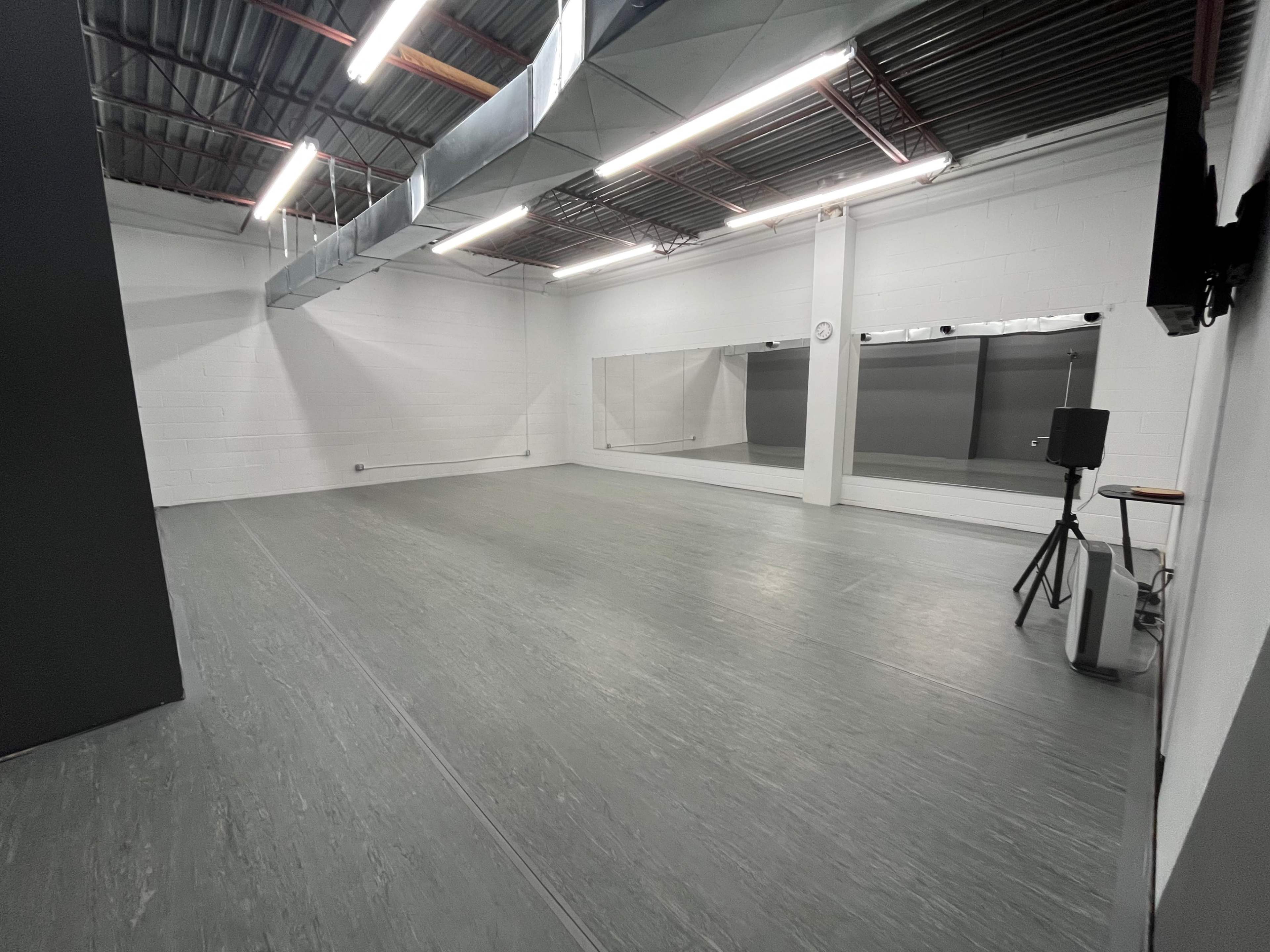 A spacious, empty studio with gray flooring, white walls, and large mirrors along one side.