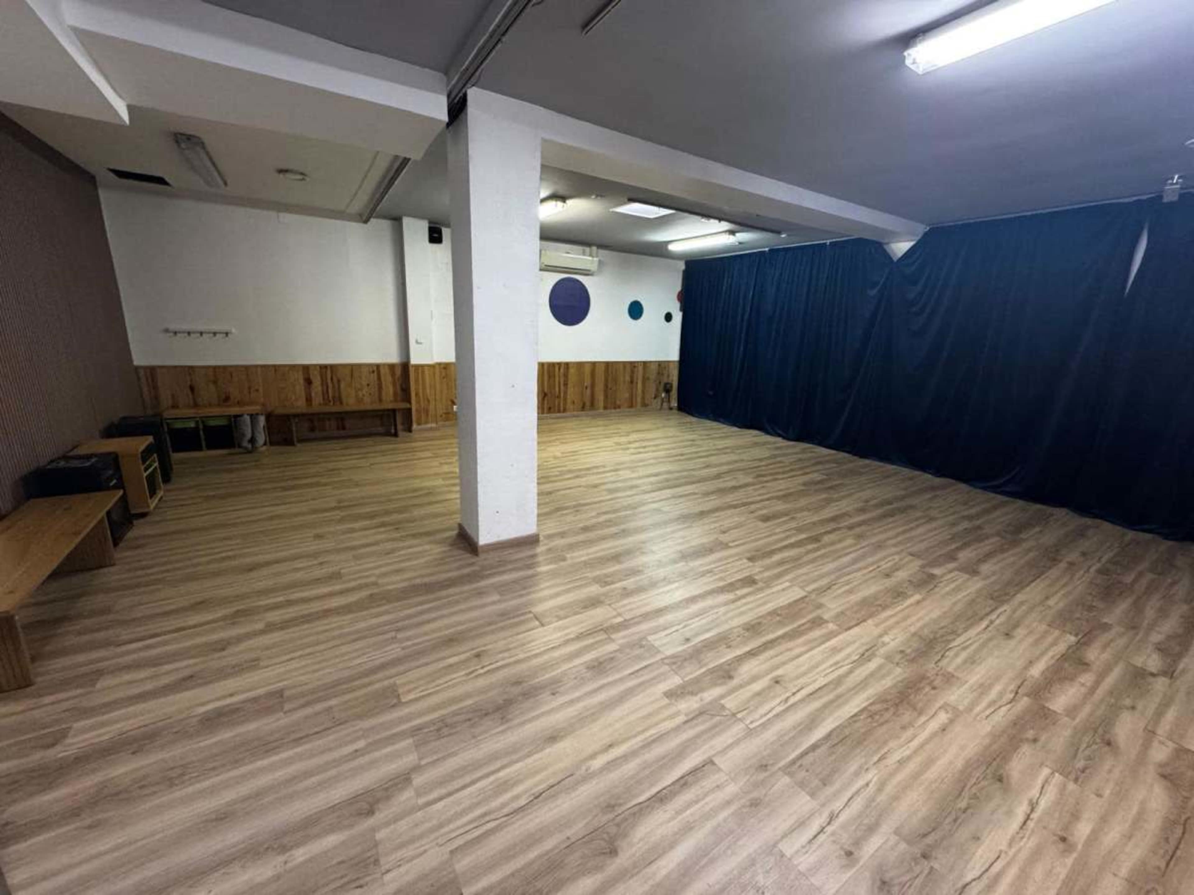 The image shows an empty room with wooden flooring, partially covered by dark curtains, and features a wooden wall panel with hooks.