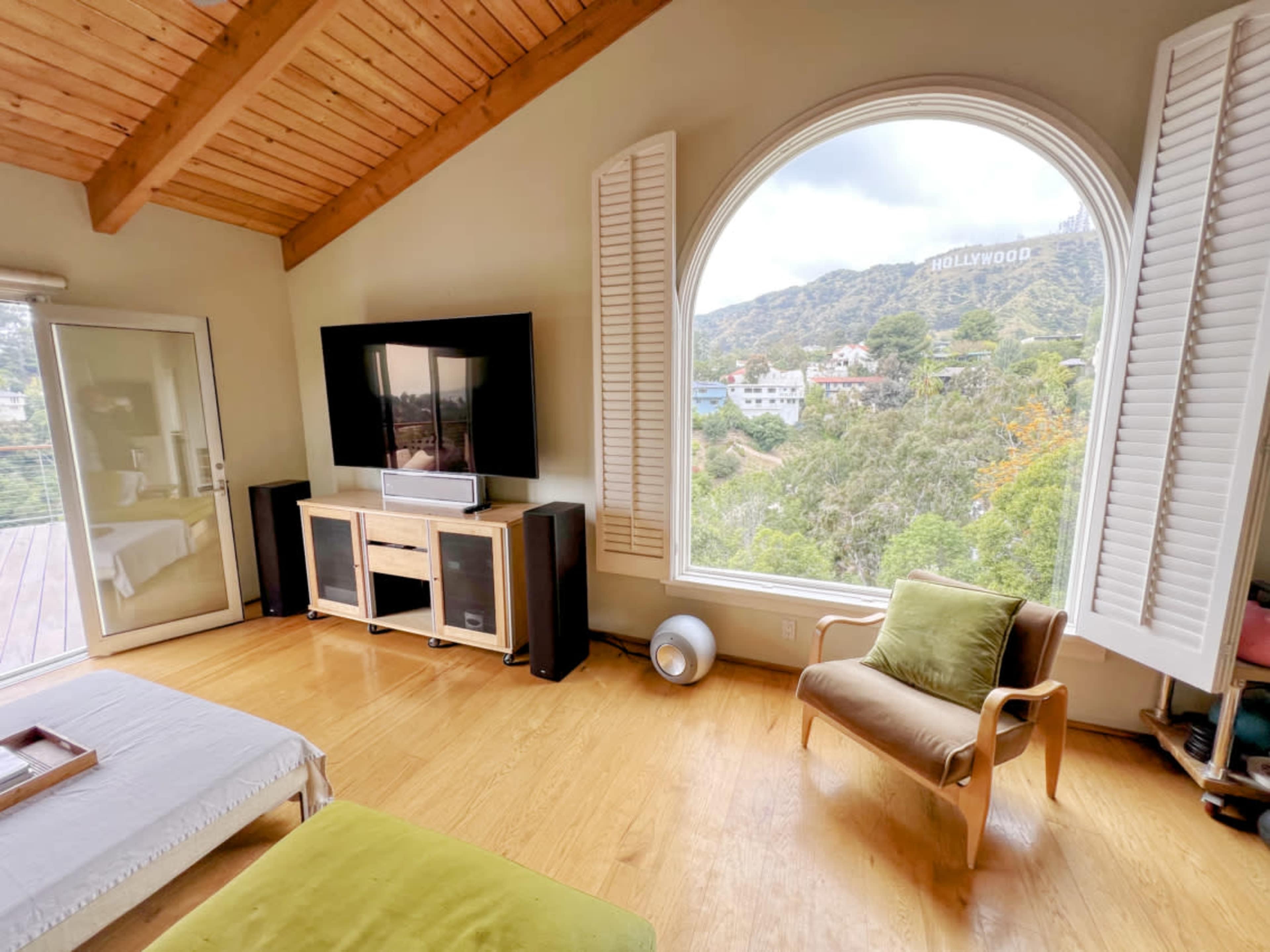 A spacious room features a large window with a view of the Hollywood sign, a television set, and a green armchair.