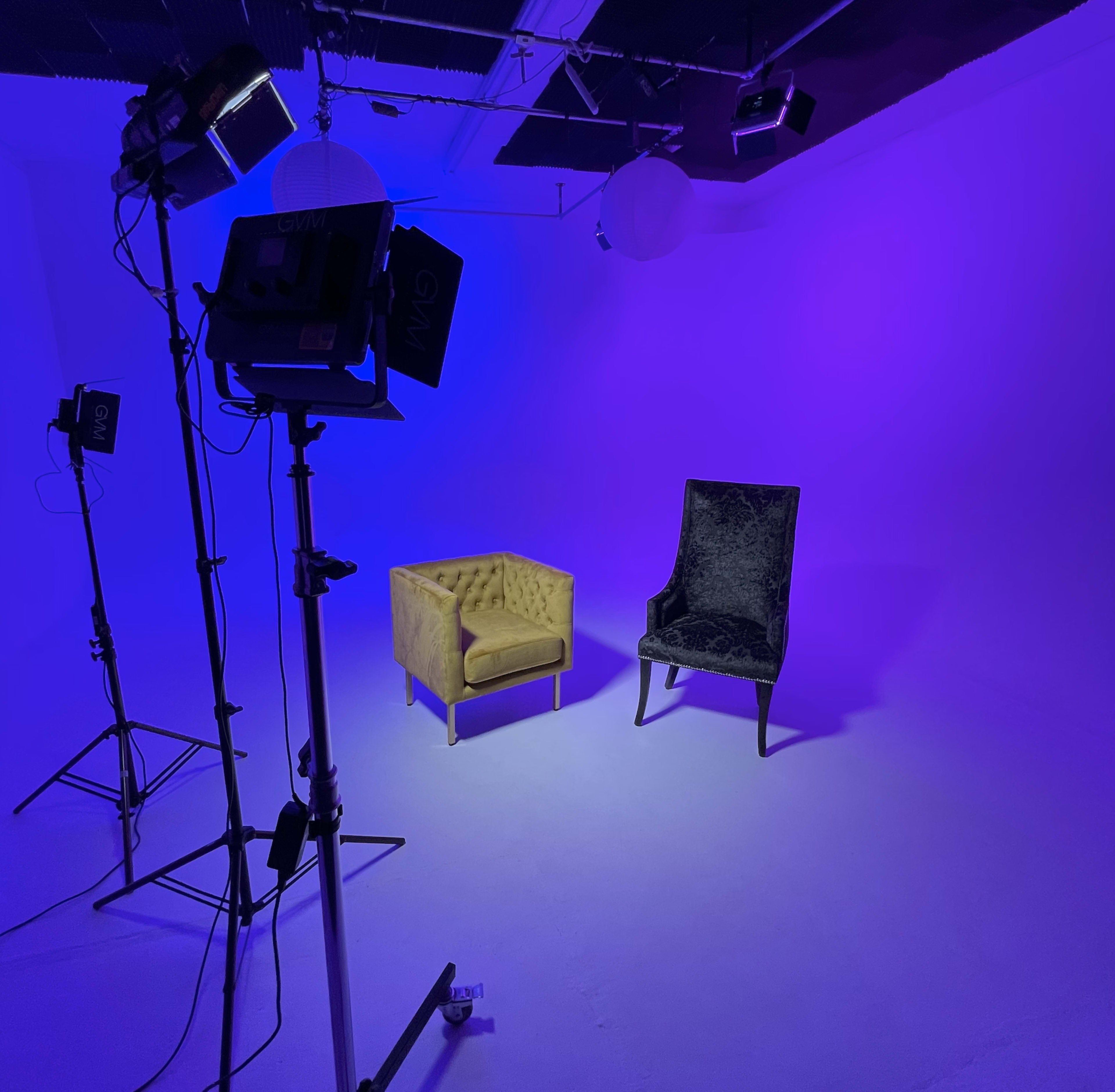 A studio setup features a yellow tufted sofa and a black upholstered chair on a purple-lit background.