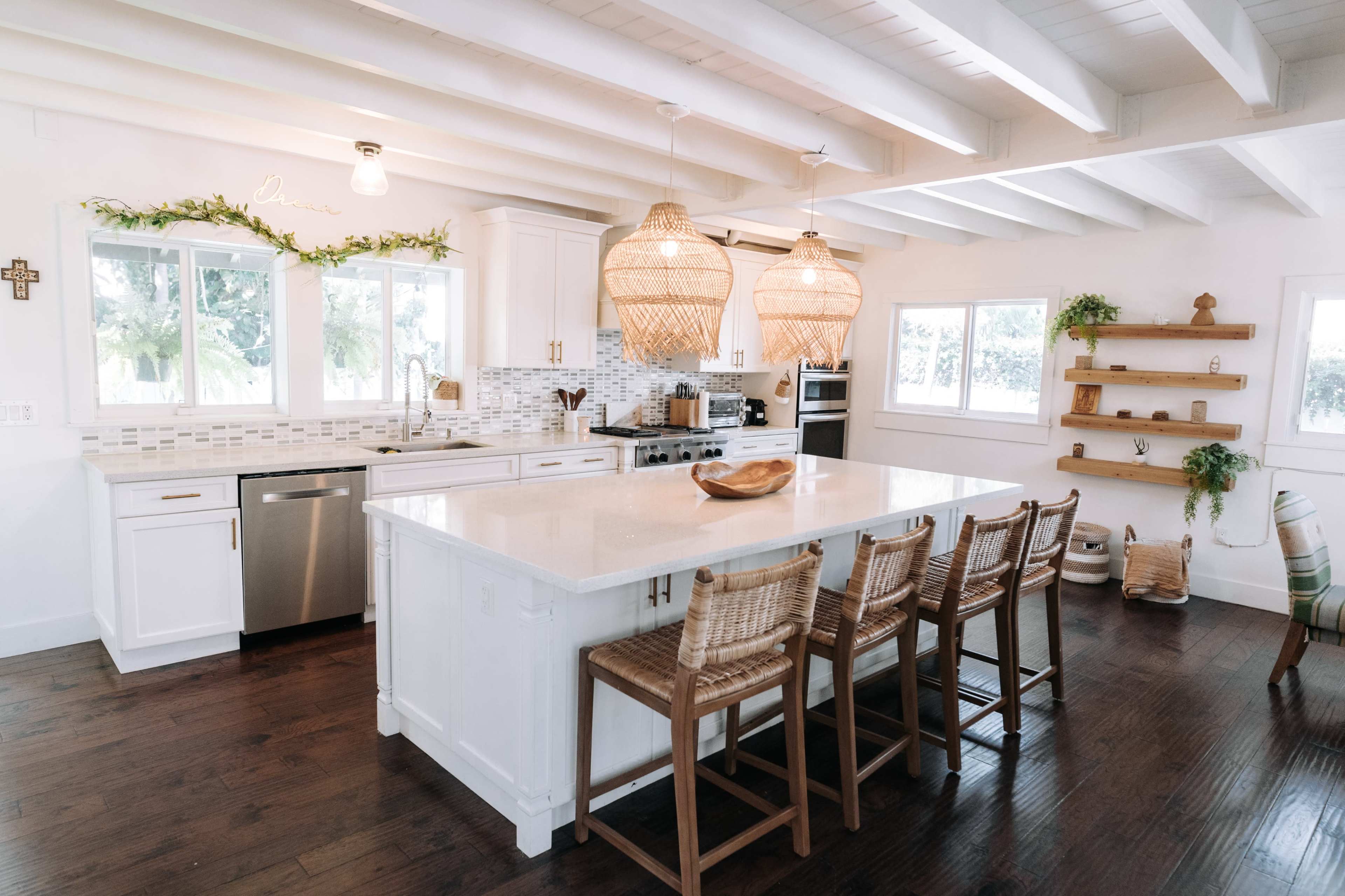 A modern kitchen with white cabinets, a large island with bar stools, and pendant lights hanging above.