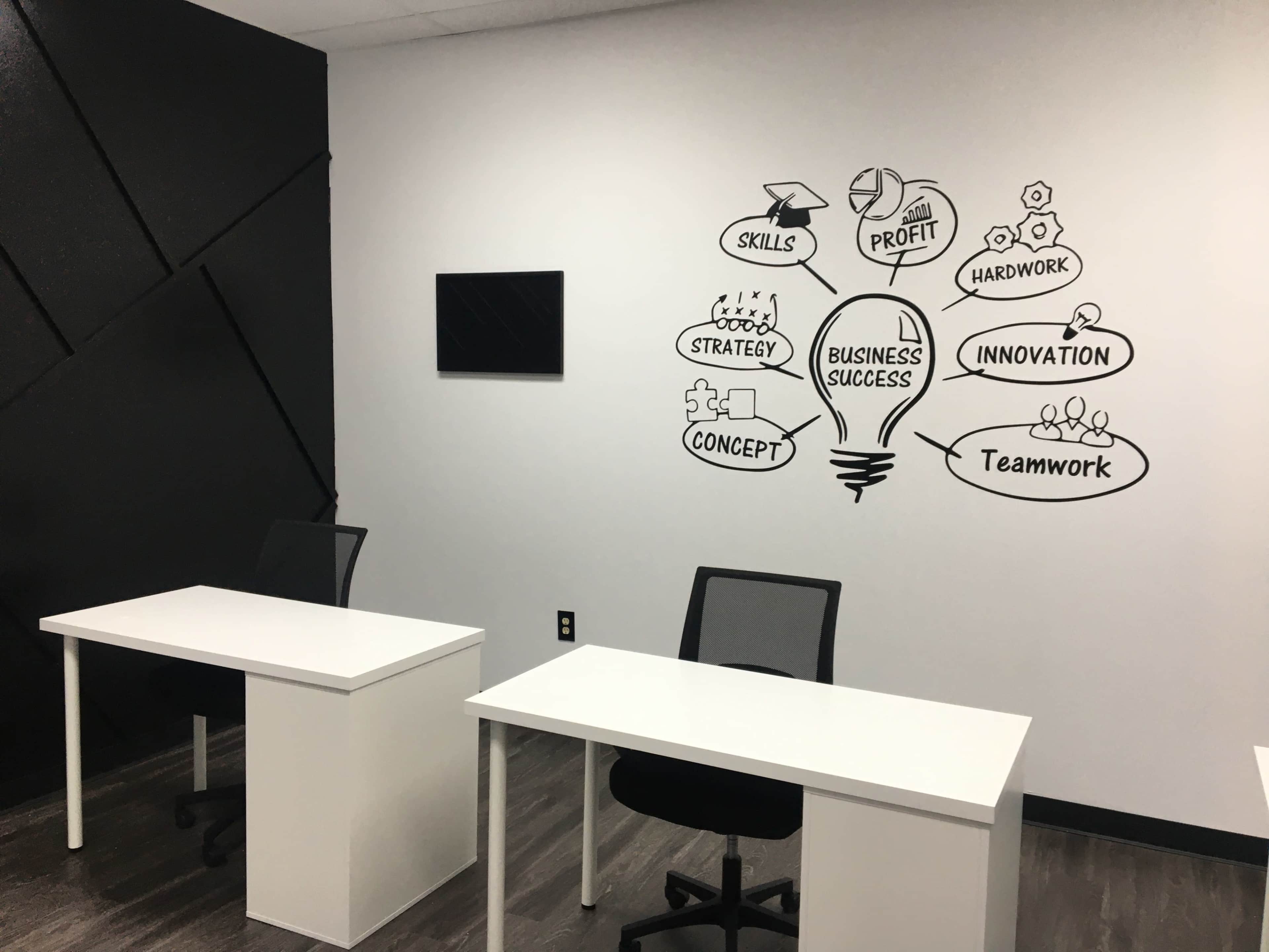 The image shows a modern office space with two white desks and a black and white mural on the wall depicting concepts related to business success.