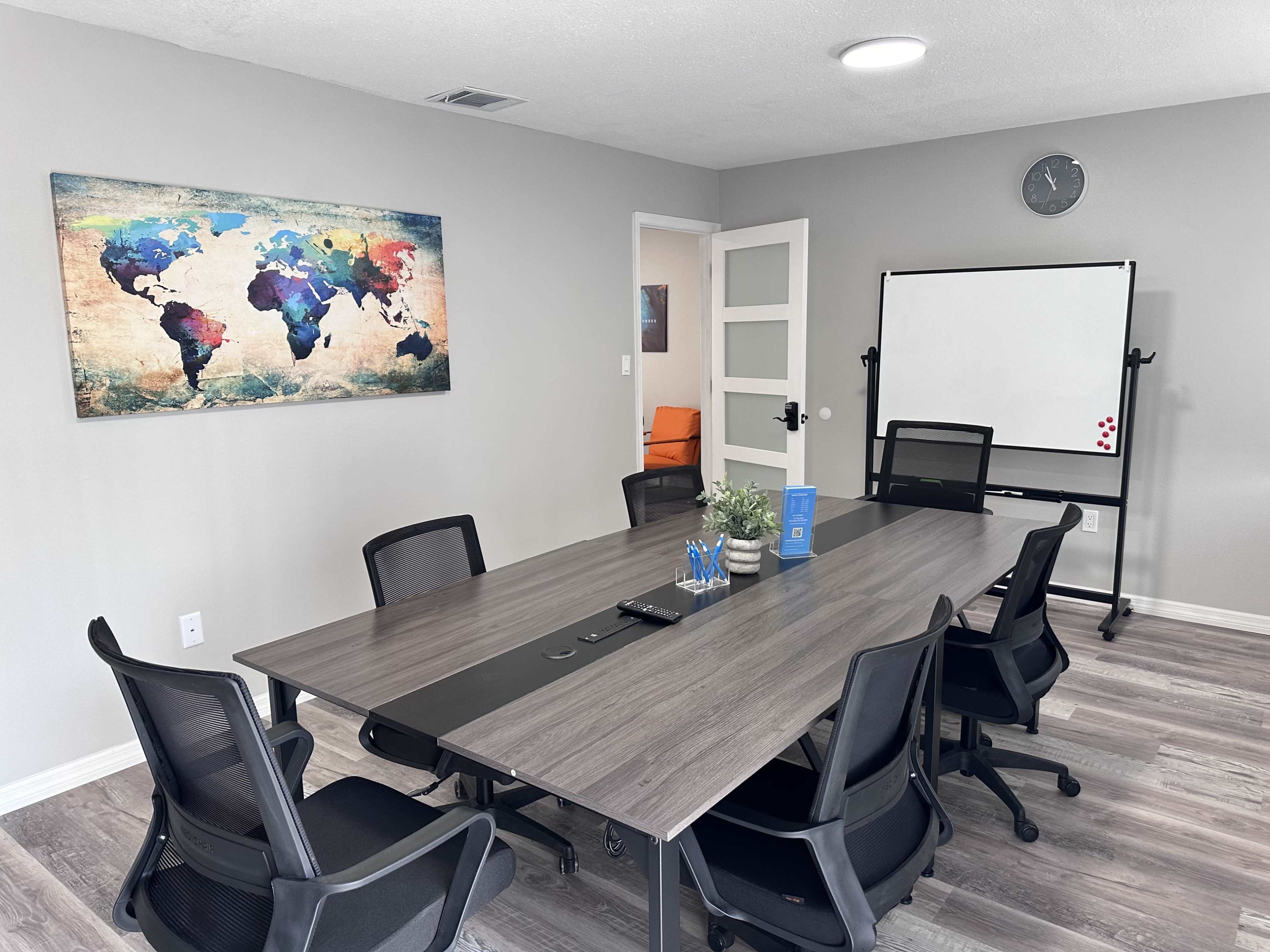 A modern conference room features a large table surrounded by black chairs, with a world map on the wall and a whiteboard nearby.