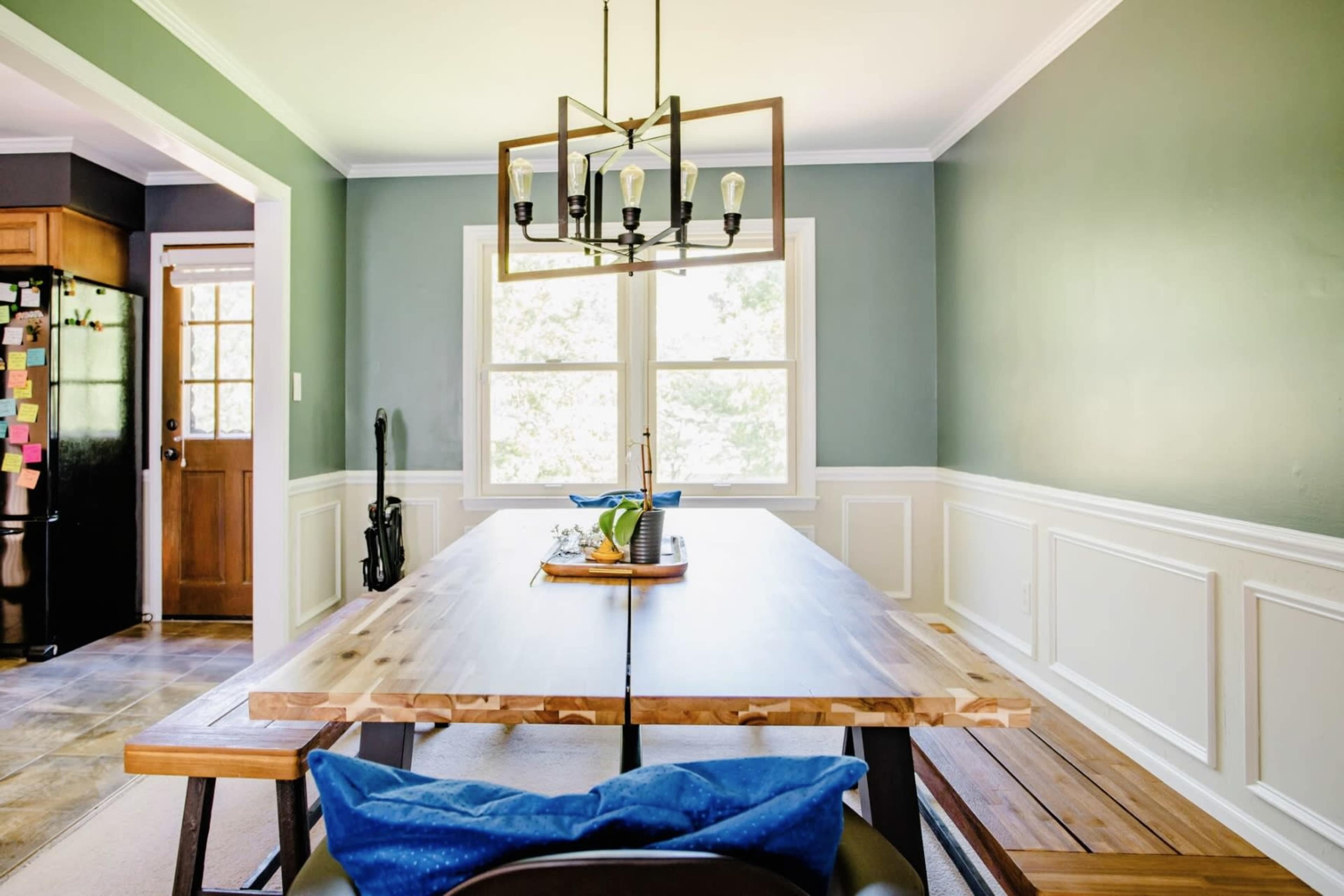A spacious dining room features a wooden table with benches, surrounded by green walls and large windows.