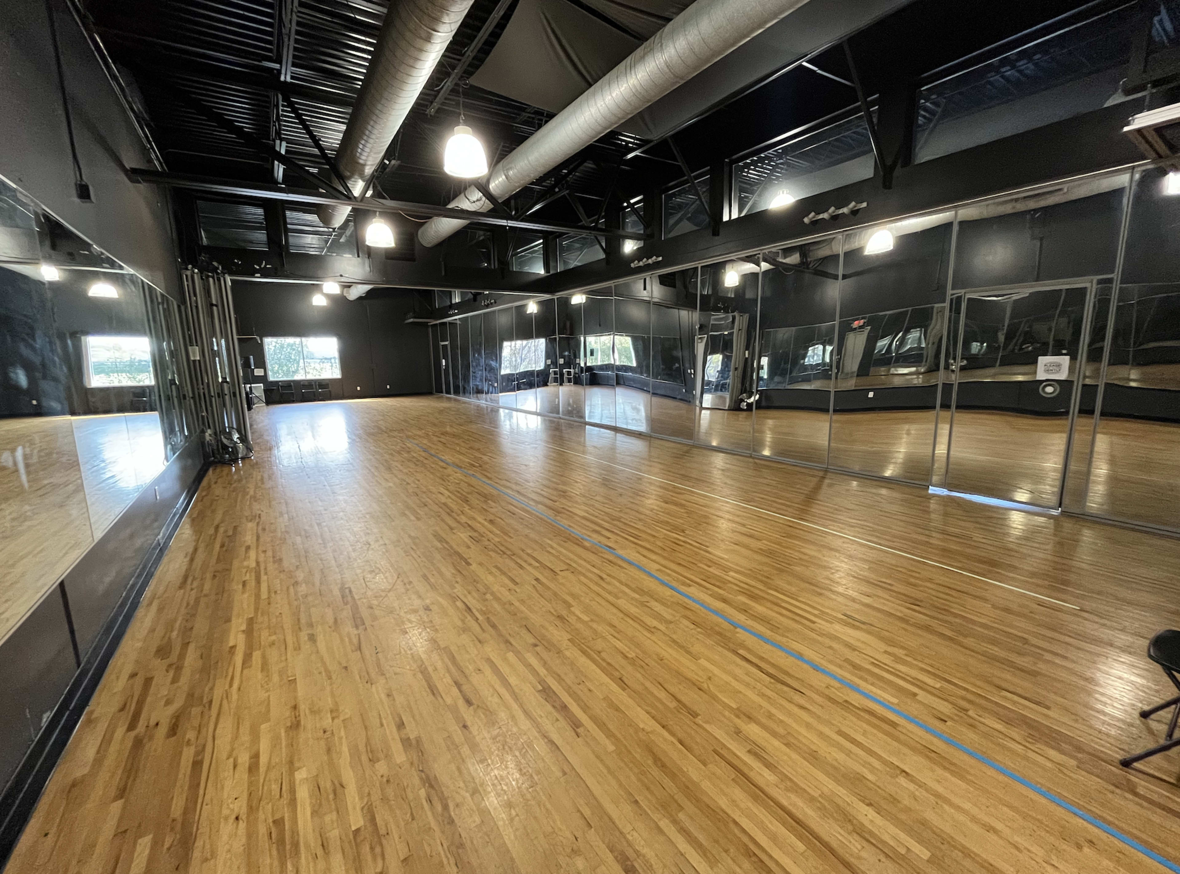 A spacious dance studio with hardwood floors and large mirrors along one wall.