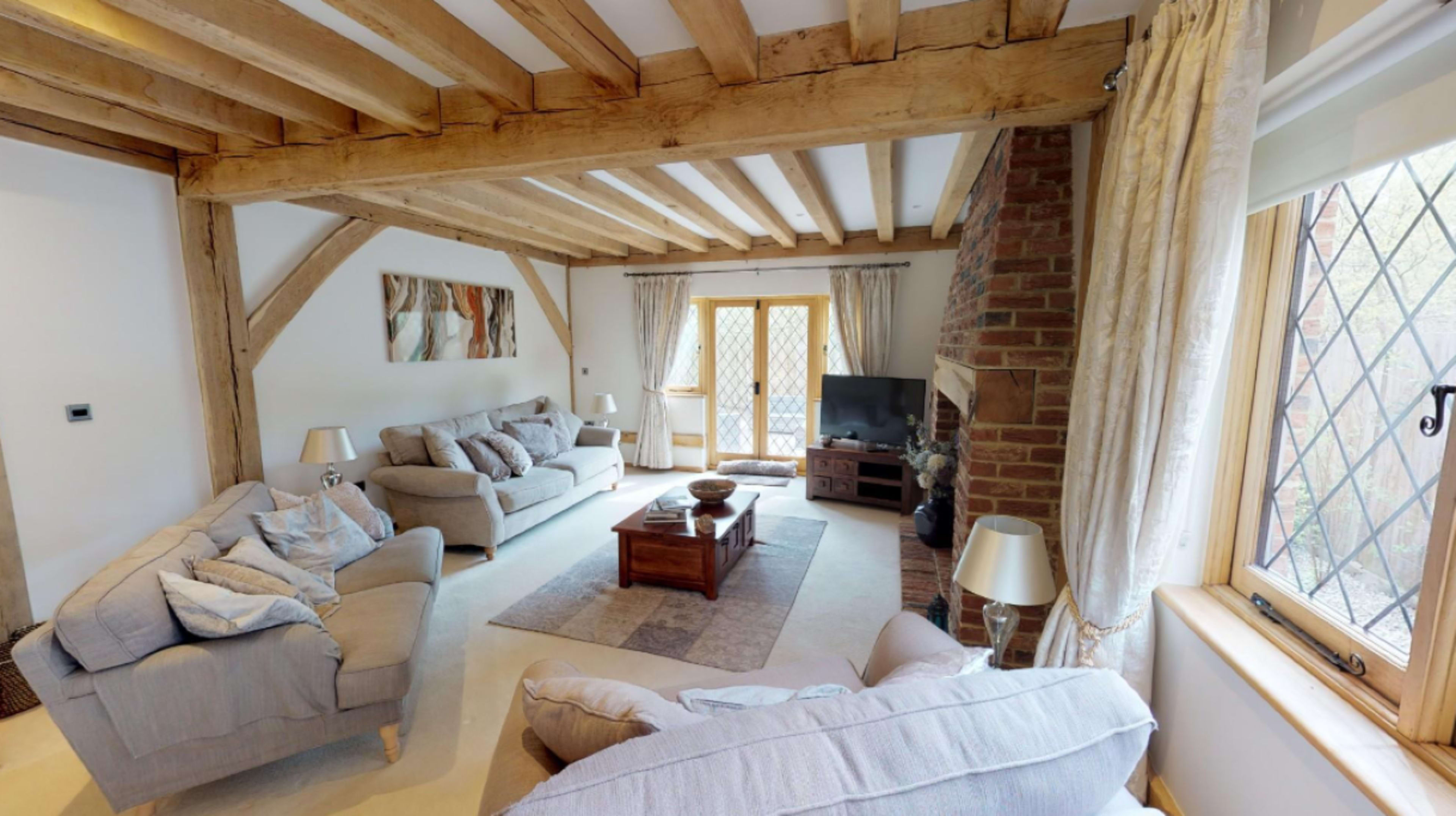 A living room with wooden beams, two sofas, a coffee table, and a television beside large windows.