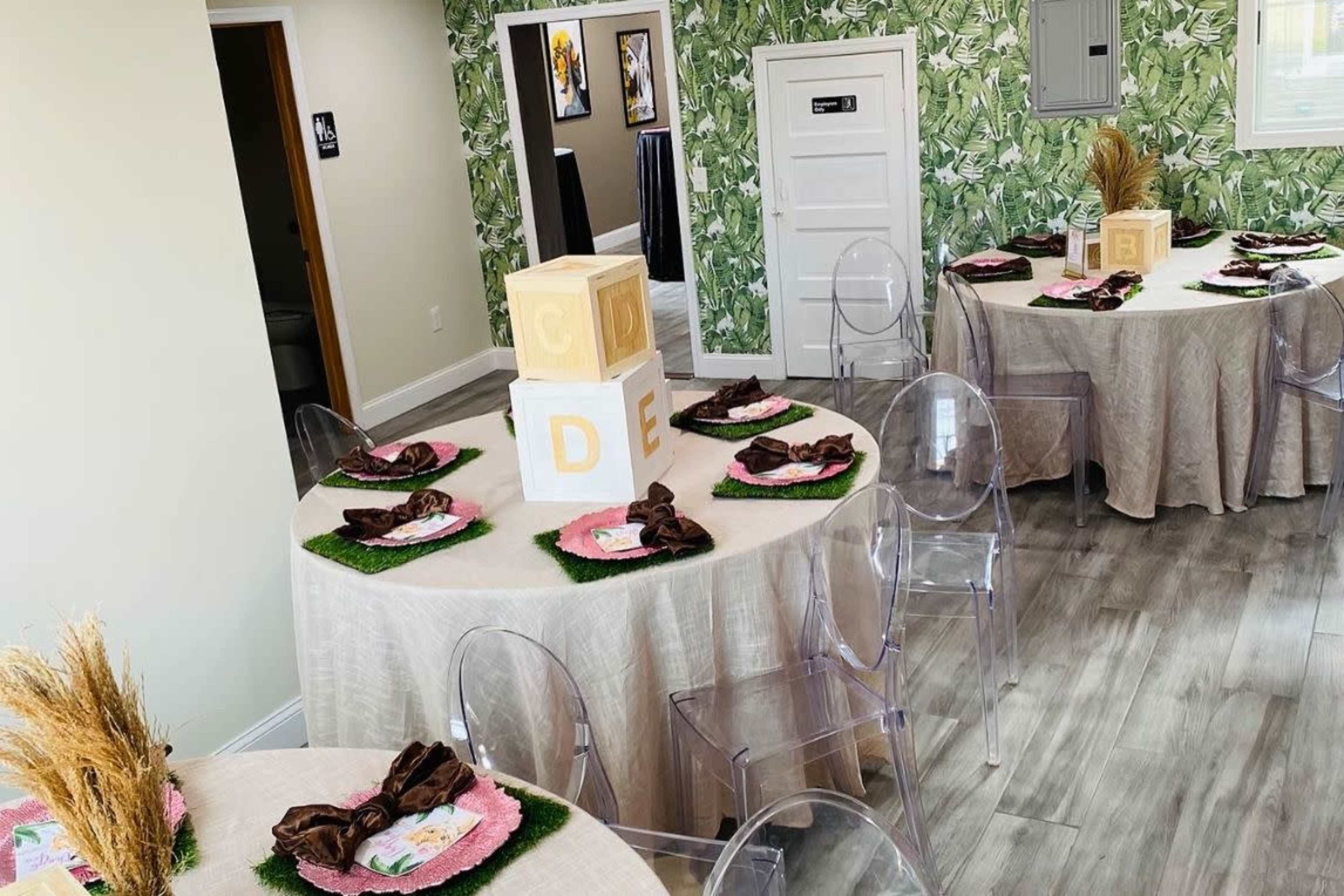 A decorated room with two round tables covered in light-colored tablecloths, each set with plates, napkins, and decor featuring wooden blocks.