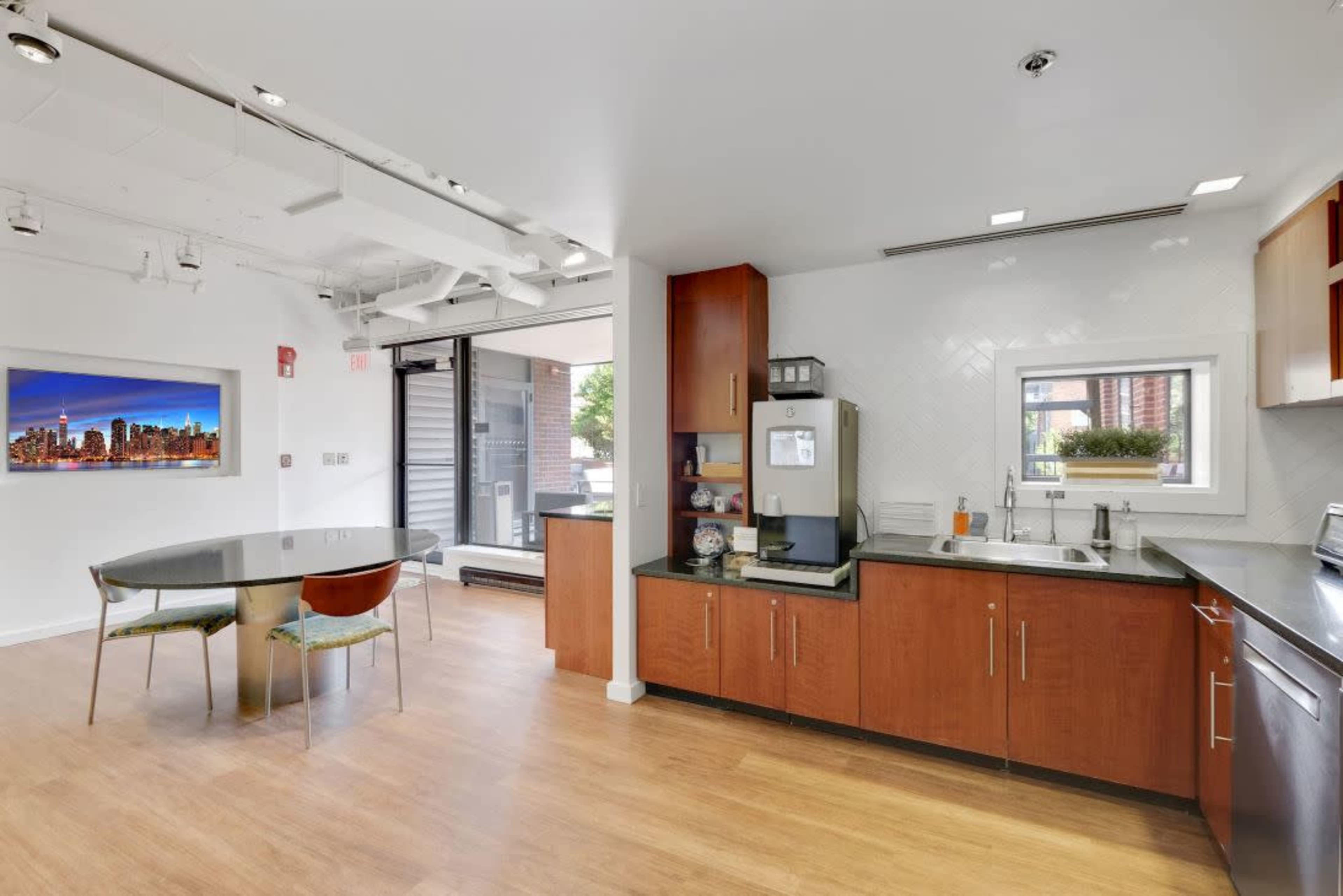 A modern kitchen with wooden cabinets, a round dining table, and a view of a cityscape through a nearby window.