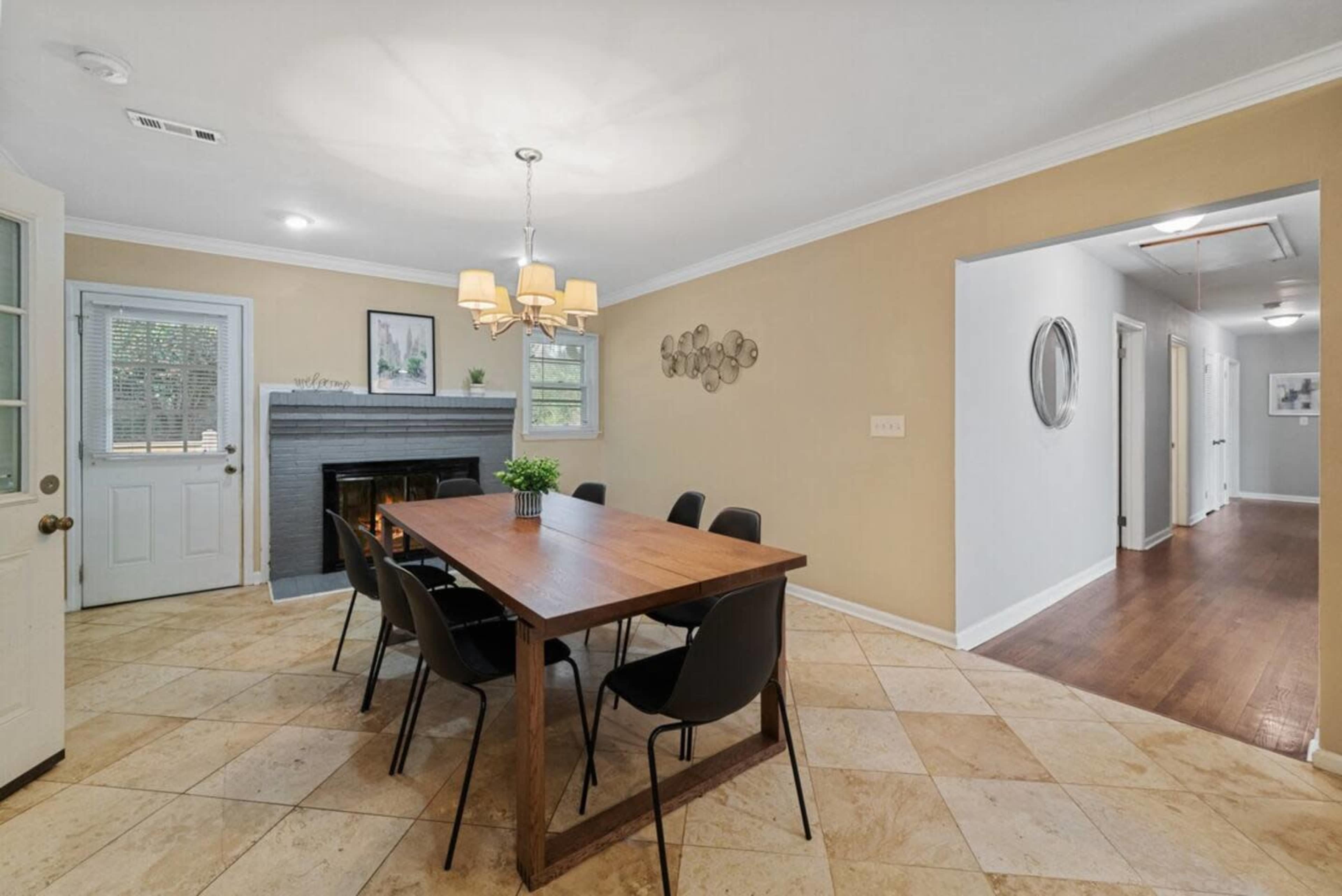 The image shows a dining area with a large wooden table surrounded by black chairs, a fireplace on one wall, and a doorway leading to a hallway.