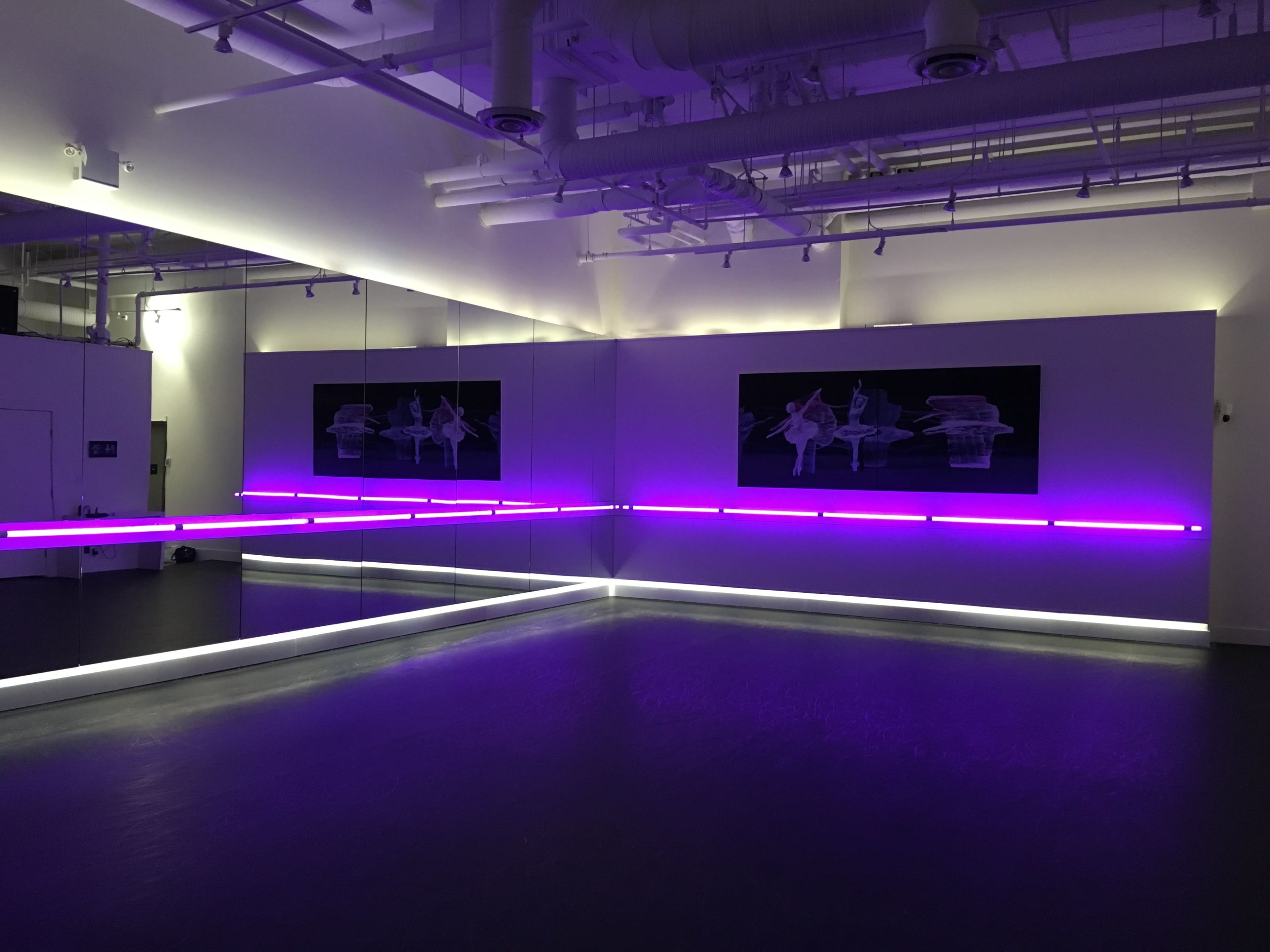 A modern dance studio with purple LED lighting and mirrored walls.