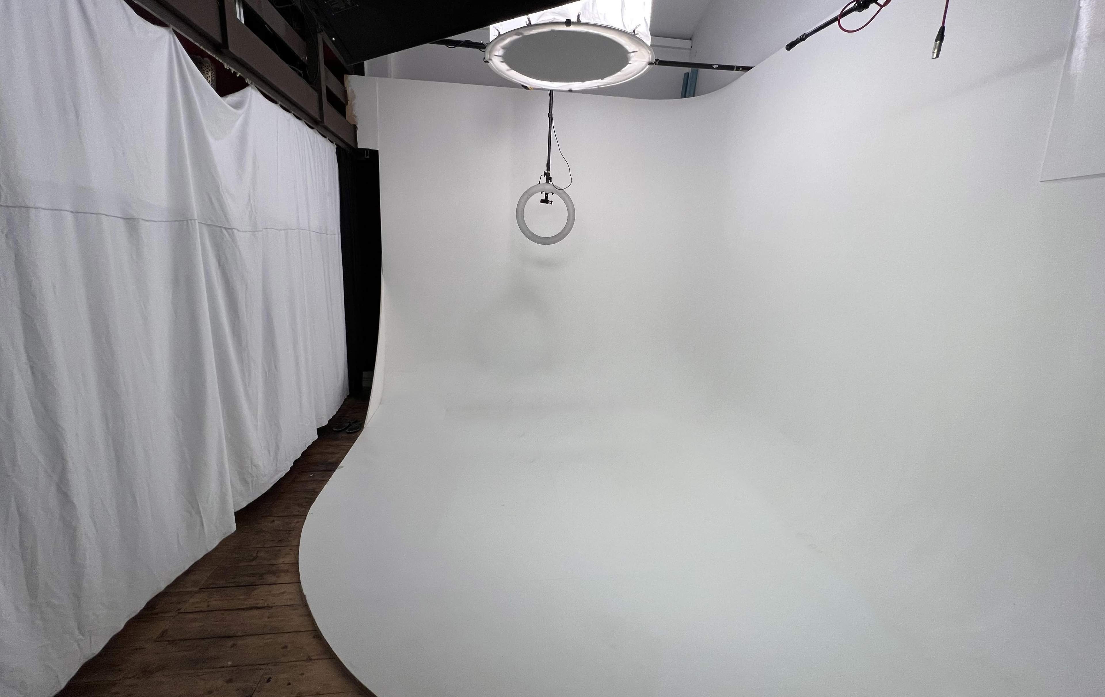 A clean, white photography studio with a curved backdrop and a circular light fixture hanging from the ceiling.