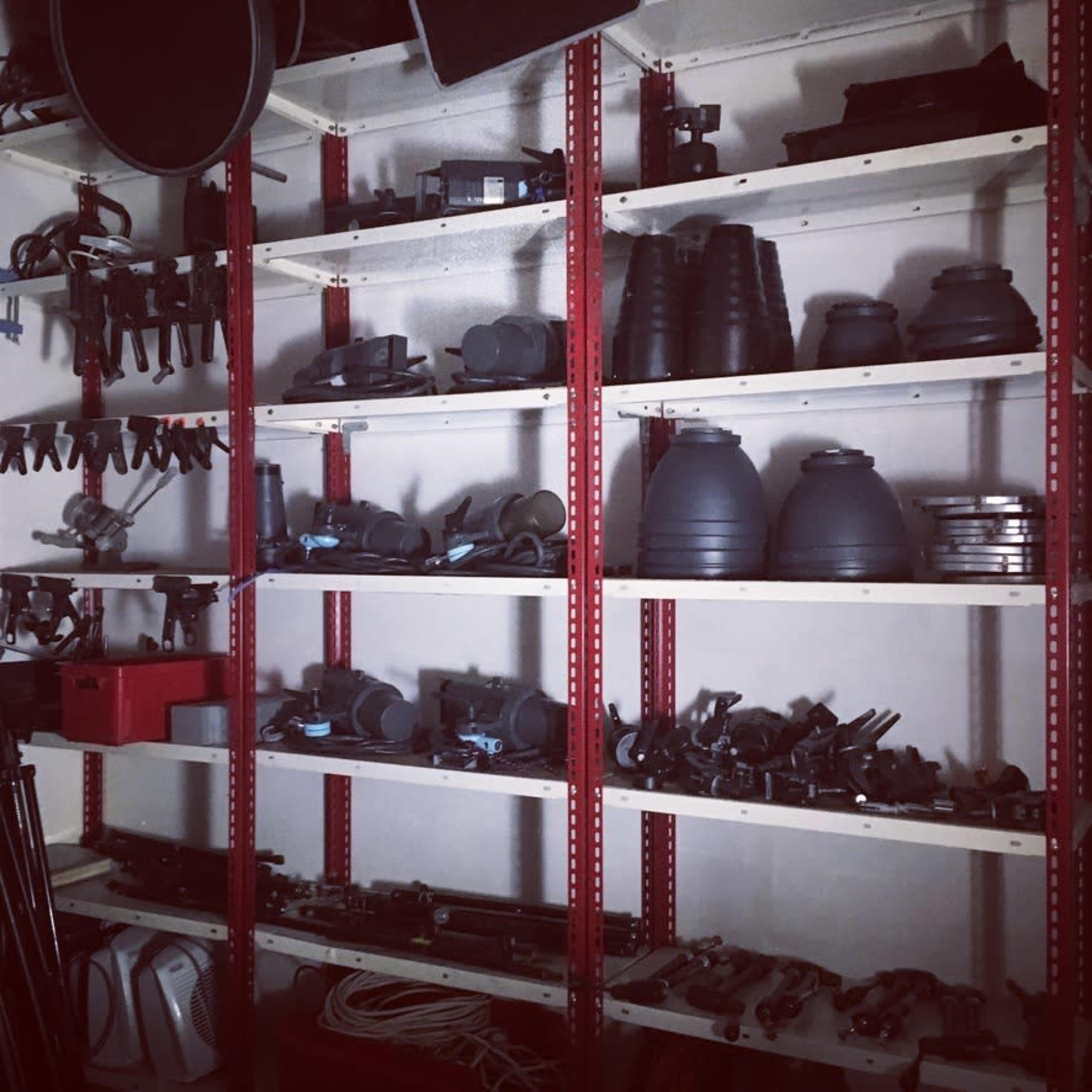 A storage area with metal shelving filled with various camera equipment and accessories, including tripods, lenses, and reels.