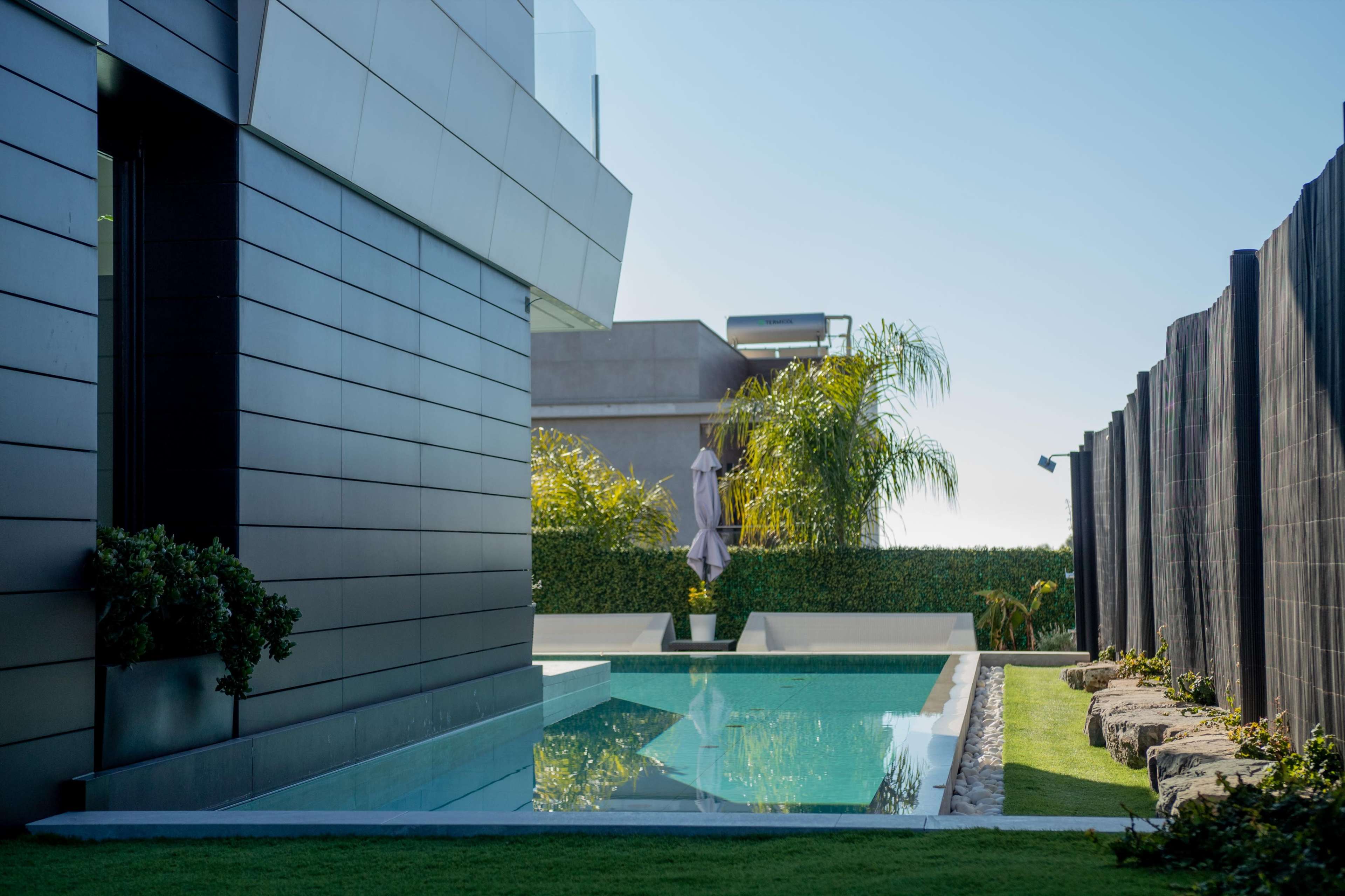 A modern house with a rectangular swimming pool and landscaped greenery in a sunny outdoor setting.