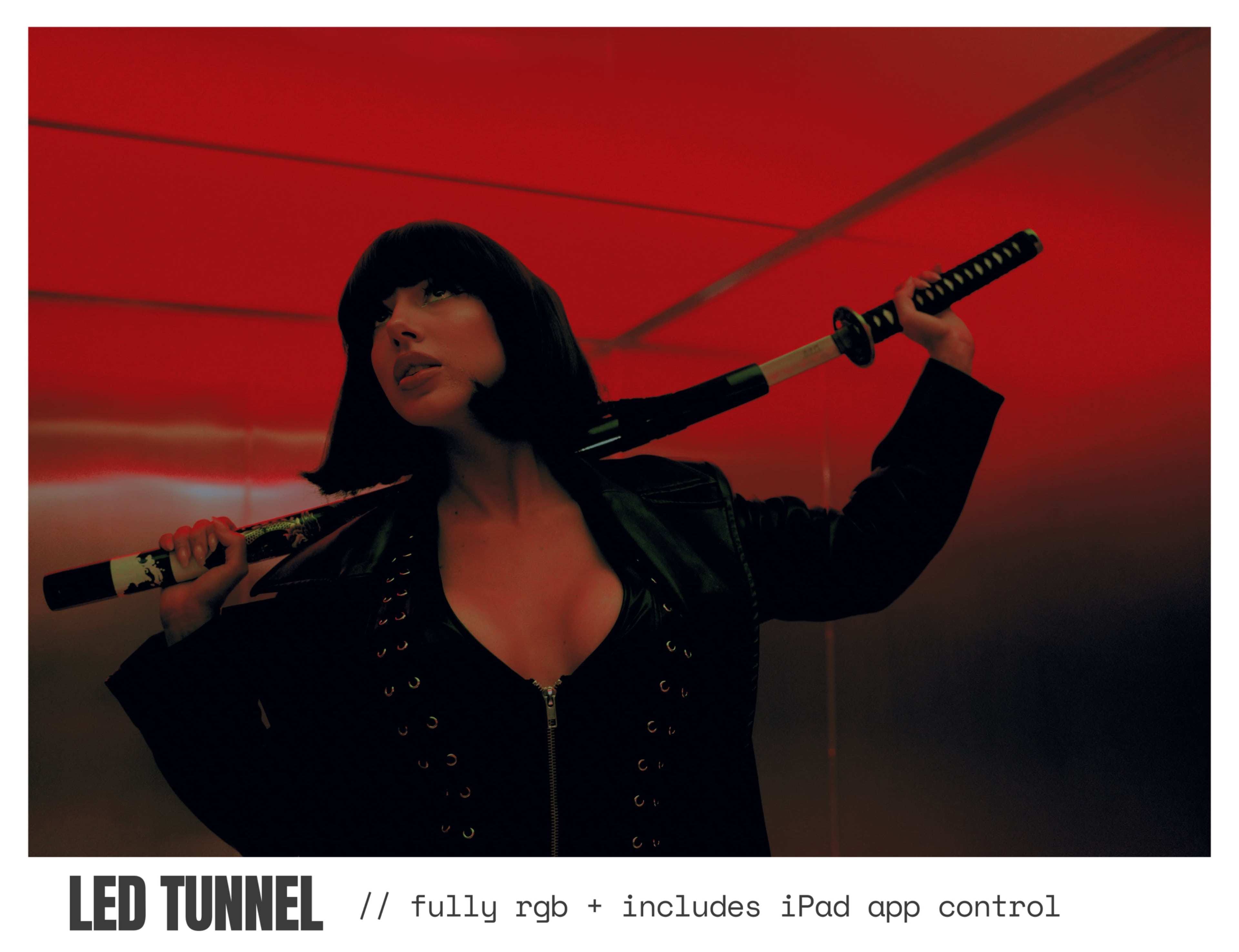A woman with a bob haircut poses in a dimly lit tunnel, holding a katana and wearing a black outfit.