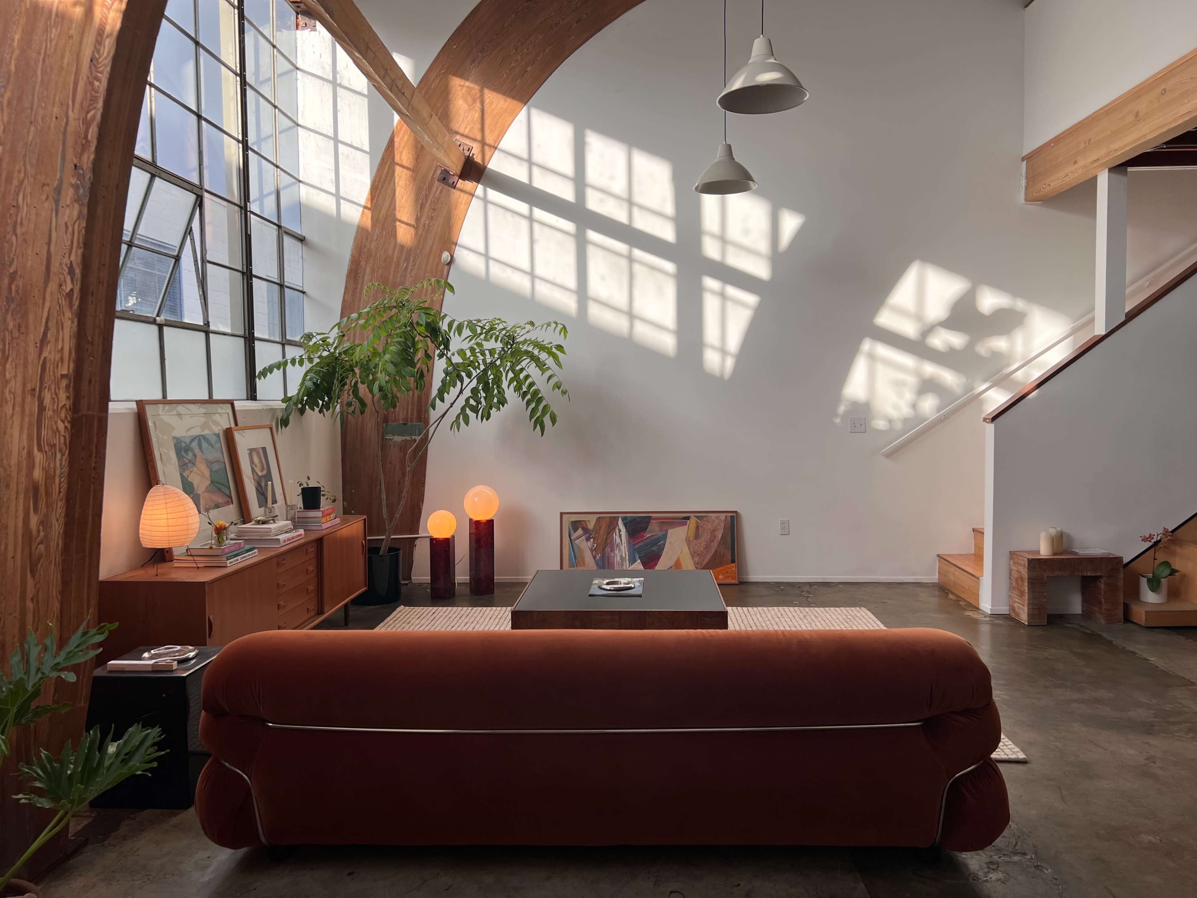 A modern living room with an orange sofa, a coffee table, and large windows casting shadows on the walls.
