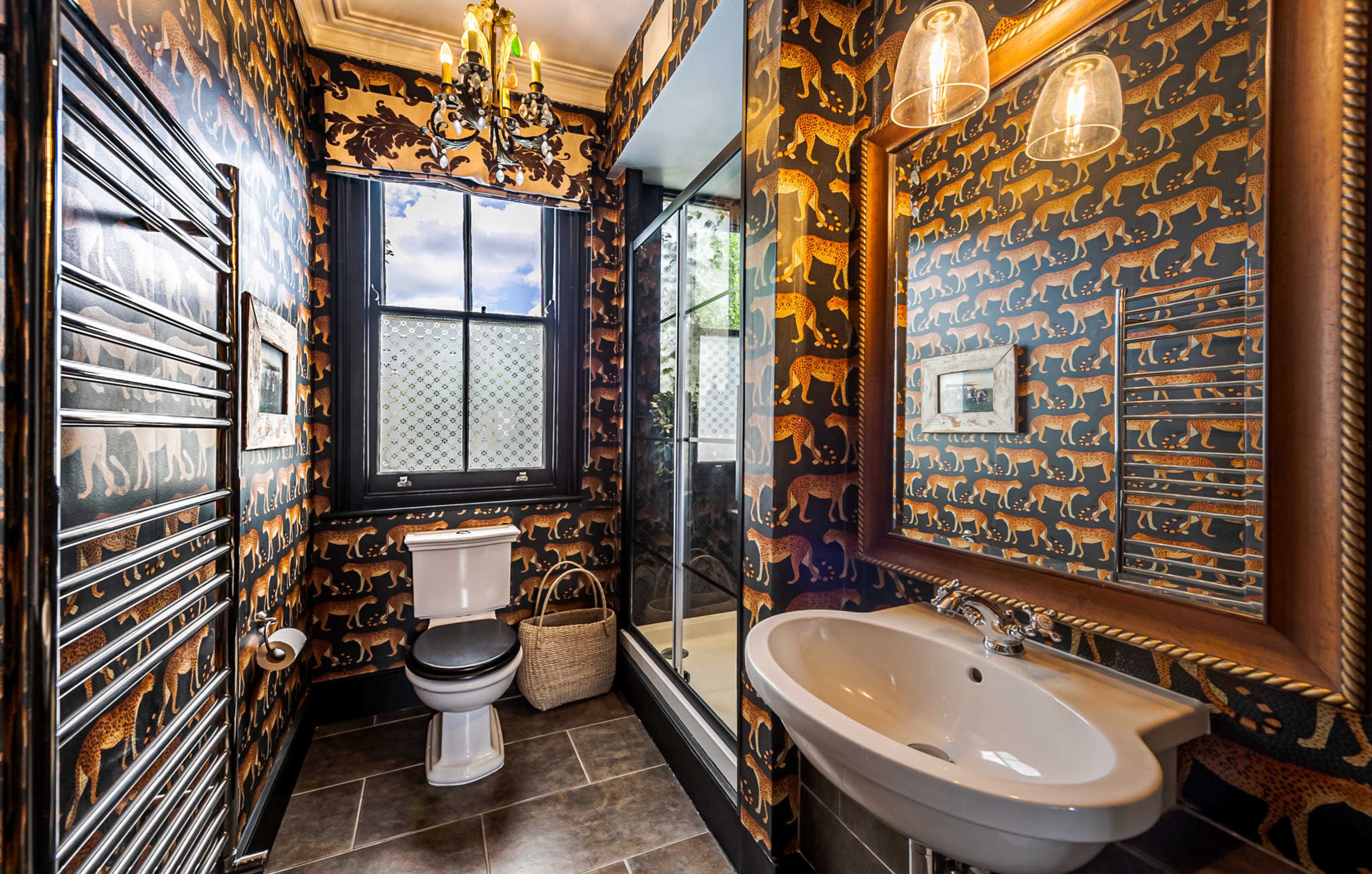 The image shows a bathroom featuring patterned wallpaper with animal motifs, a glass shower enclosure, a modern sink, and a black heated towel rail.