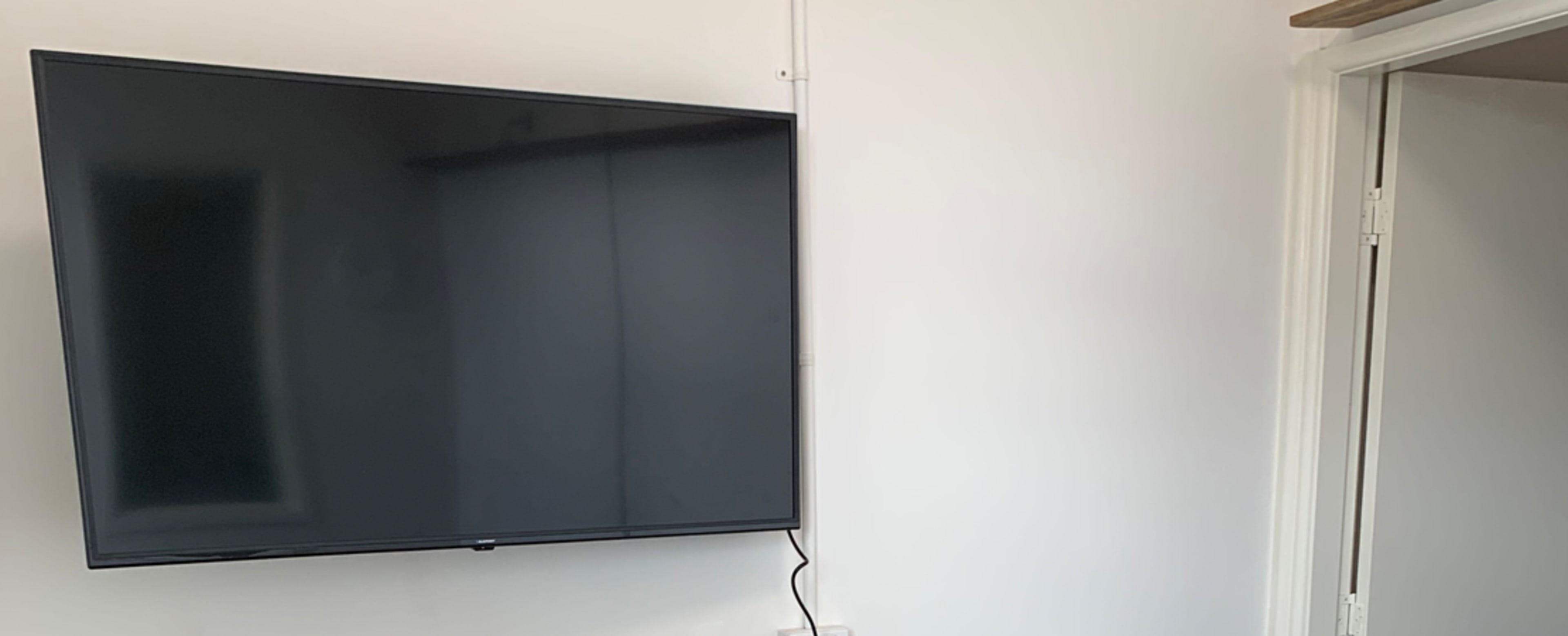 A flat-screen television is mounted on a white wall near an open door.