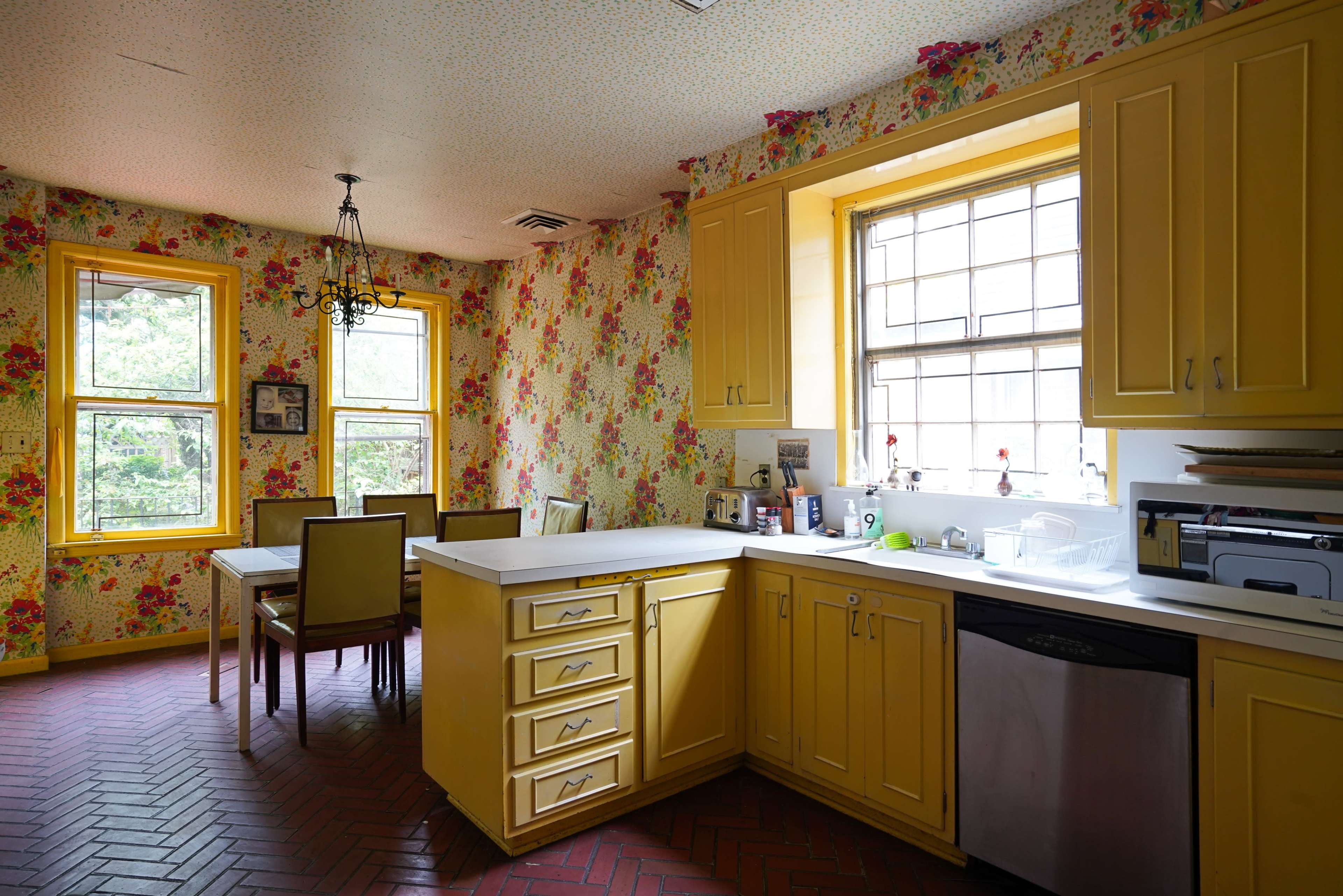 A bright, retro kitchen features yellow cabinets, floral wallpaper, a white countertop, and a dining table with four chairs.
