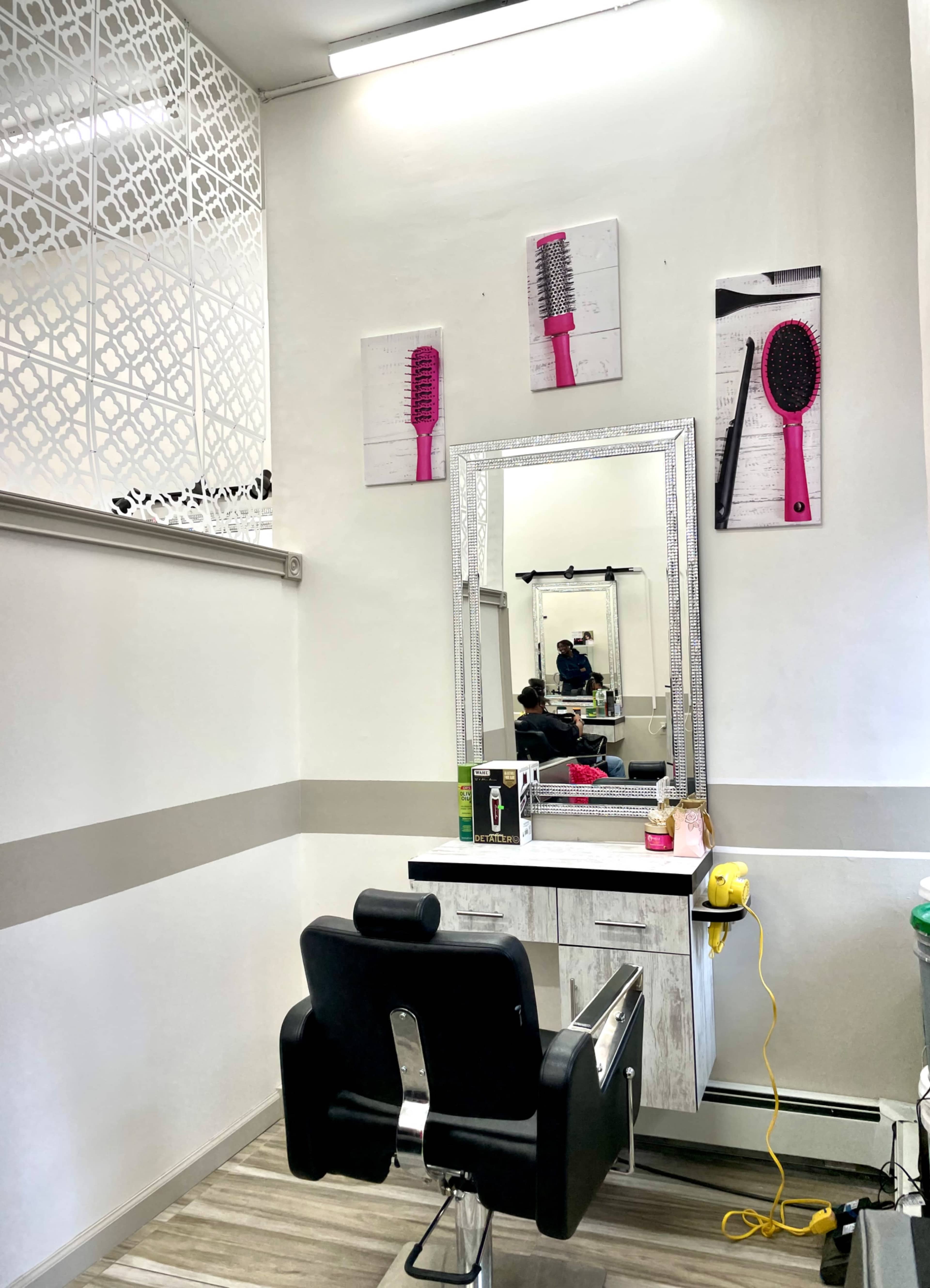 The image shows a hair salon interior featuring a styling chair, a mirror, and pink hairbrushes displayed on the walls.