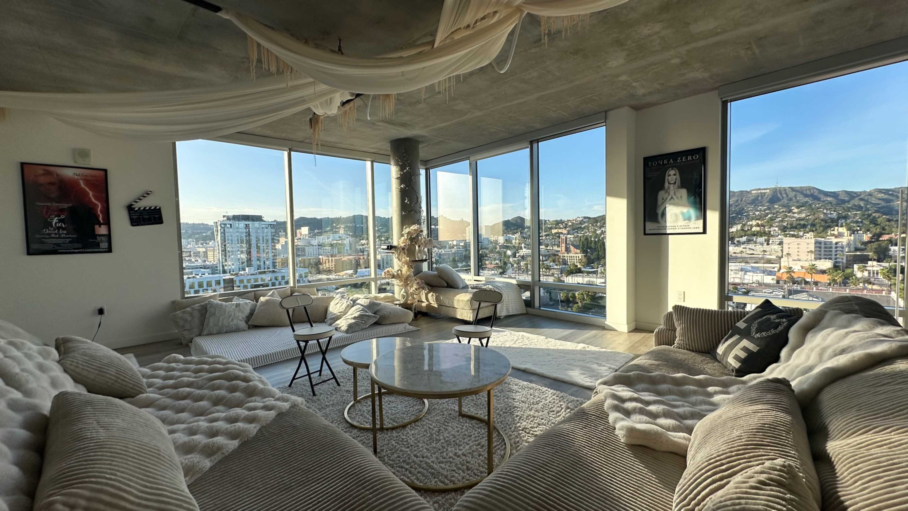 A spacious living room with large windows offers a panoramic view of a cityscape, featuring modern furniture and decorative accents.
