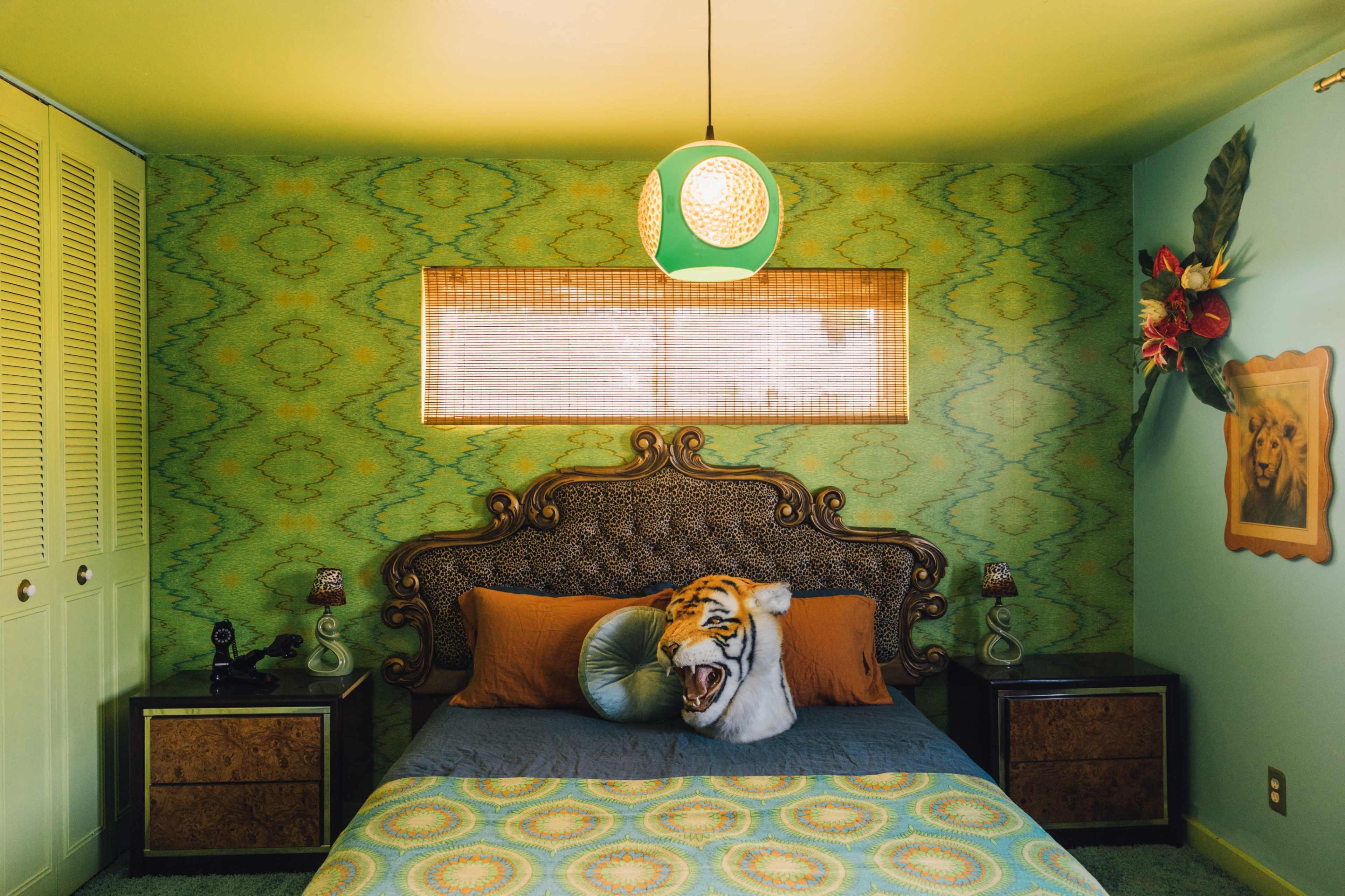 The room features a bed with a tiger-themed decorative pillow against a green and blue patterned wallpaper and a unique pendant light.