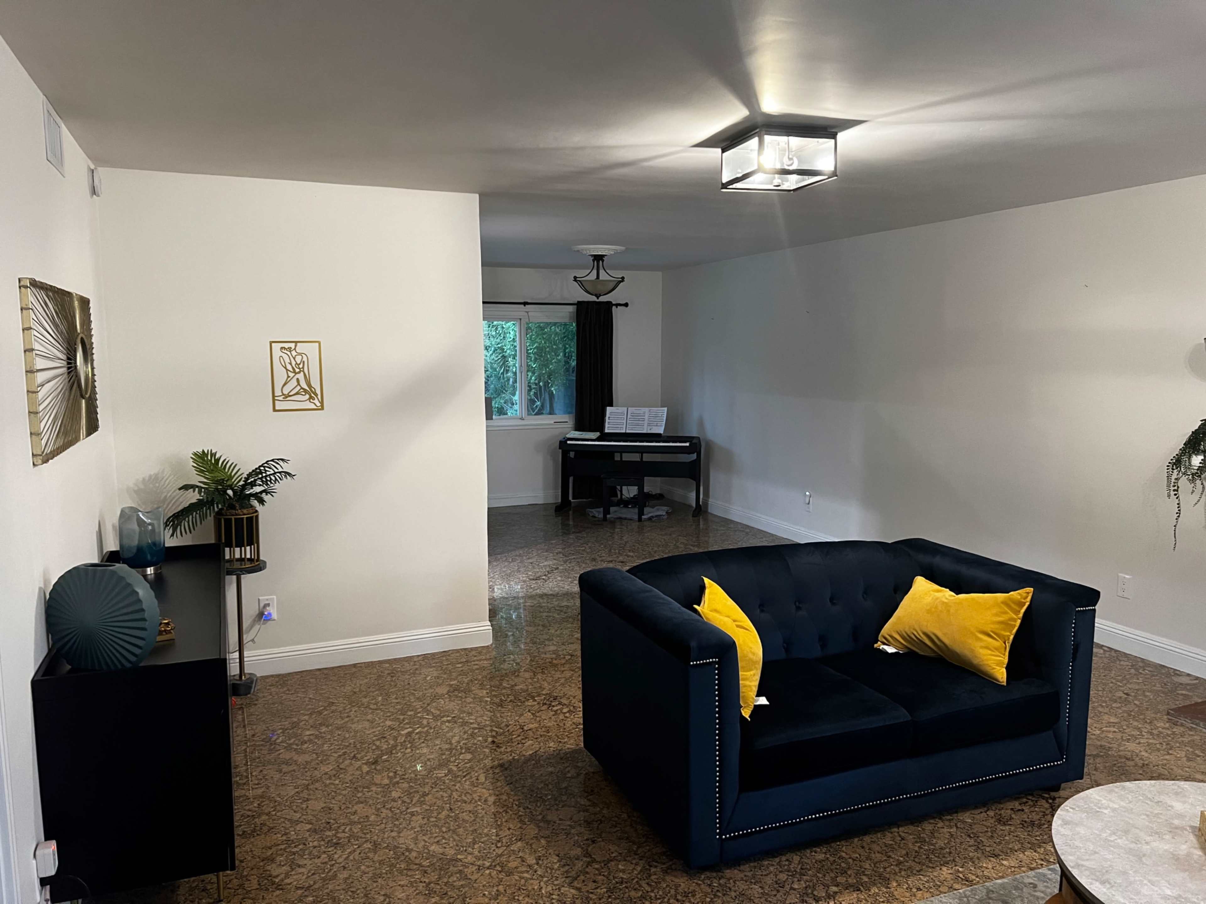 A living room with a dark sofa adorned with yellow cushions, a side table, and a piano placed in a separate area.