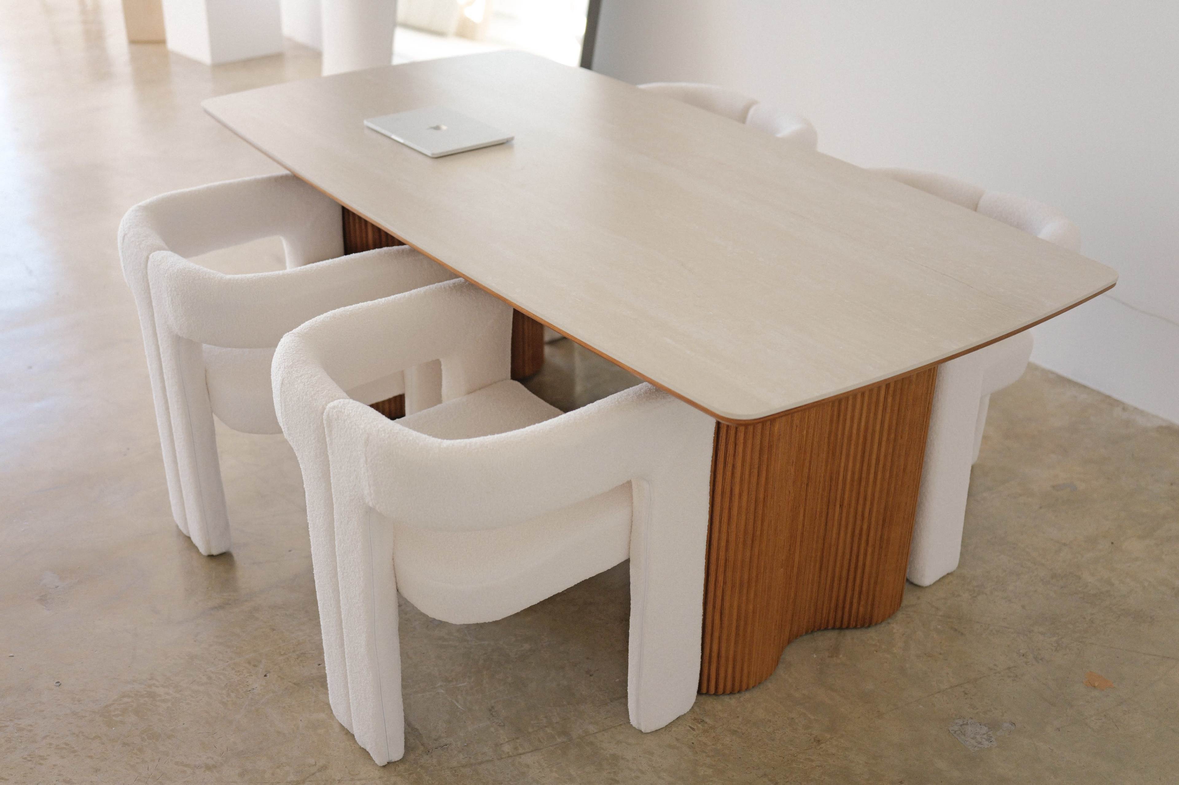 A modern dining table with a light-colored tabletop and four upholstered chairs sits on a polished concrete floor.