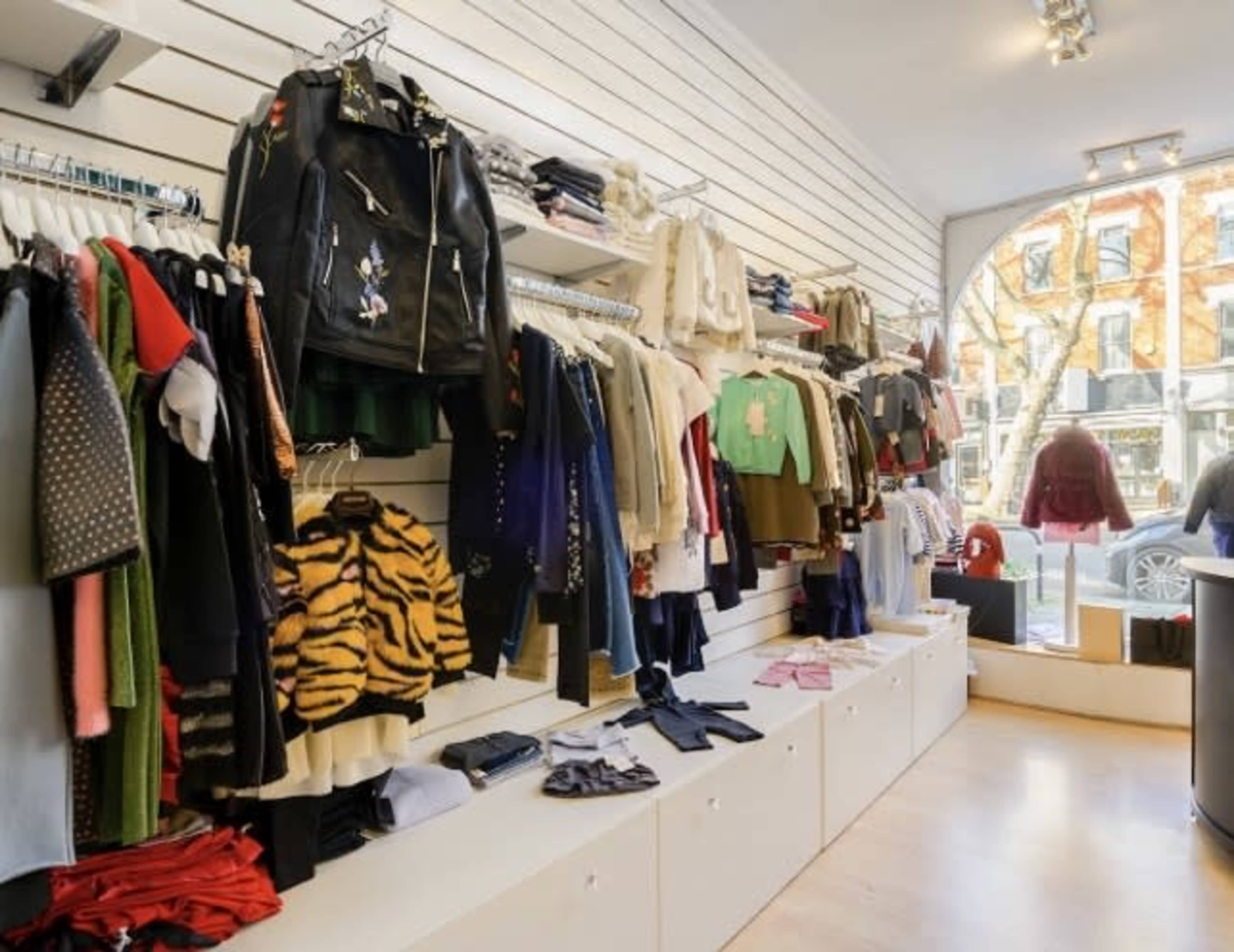 The image shows a clothing retail store with various garments displayed on wall racks and shelves, and a large window facing the street.