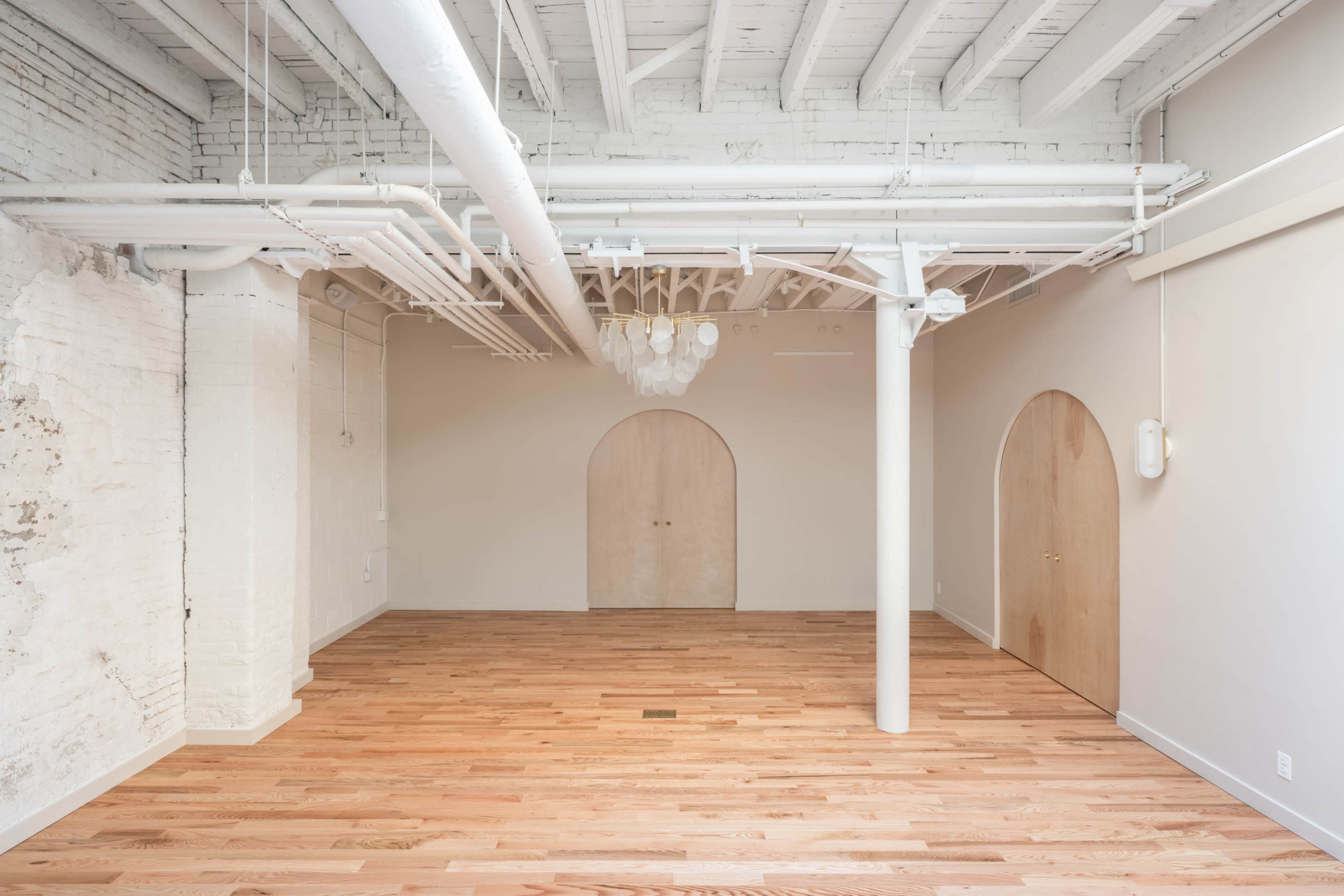 A spacious, minimalist interior with wooden flooring, exposed white beams, and two arched doorways.