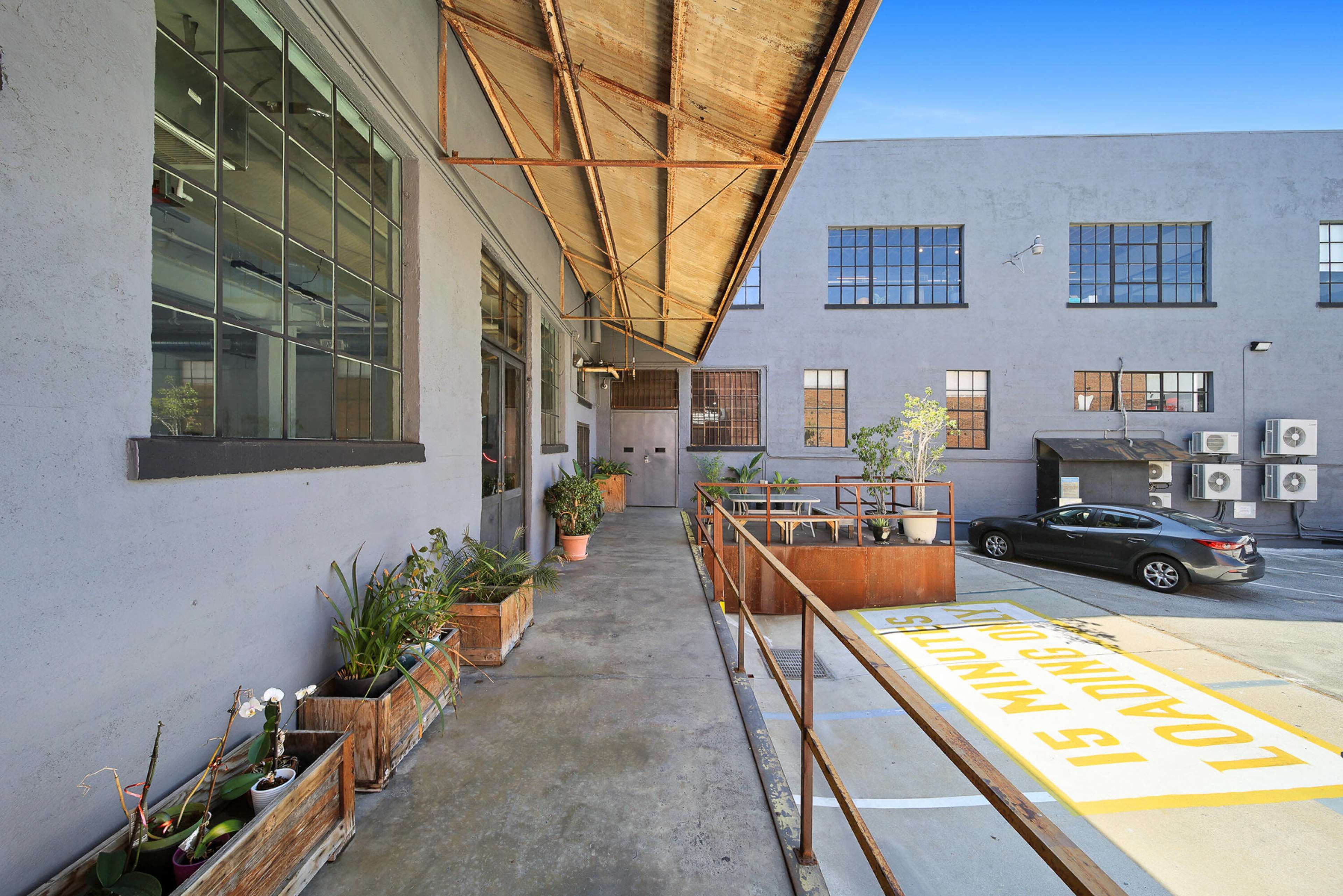 The image shows a loading area next to a warehouse with large windows and potted plants along the walkway.