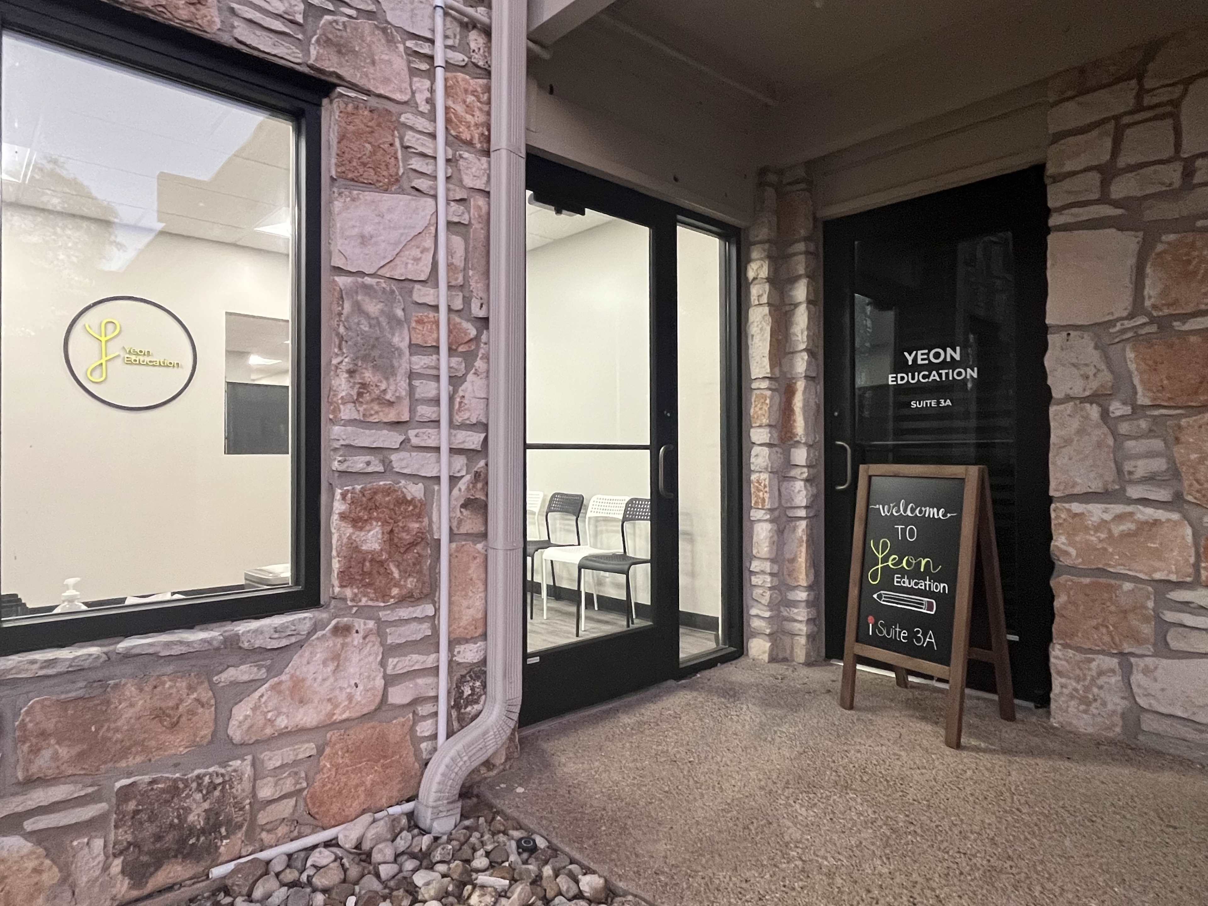 The entrance to Yeon Education features a stone wall and a sign indicating the suite number, with chairs visible inside the facility.