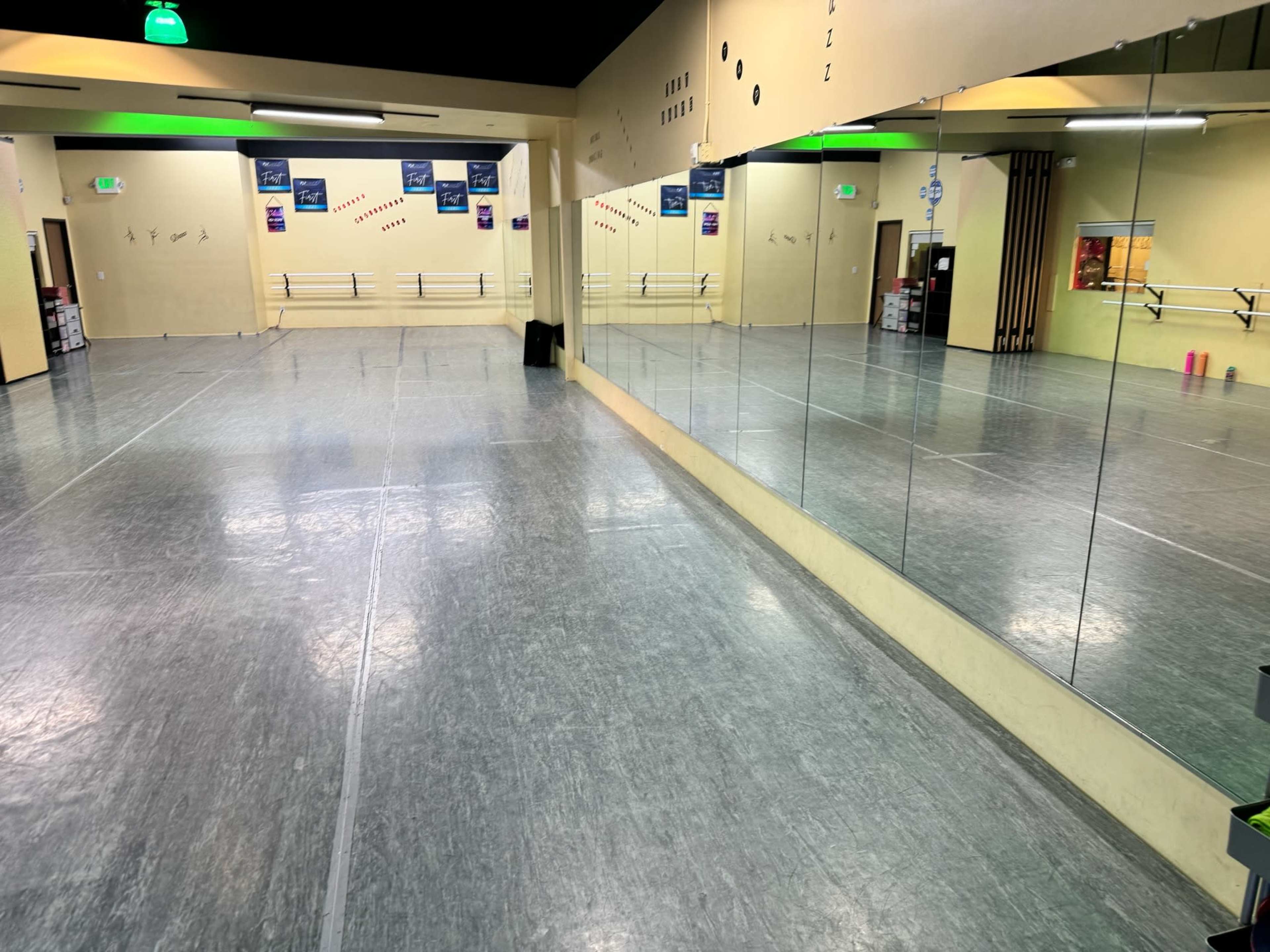 A spacious dance studio with a mirrored wall and a smooth, gray floor.