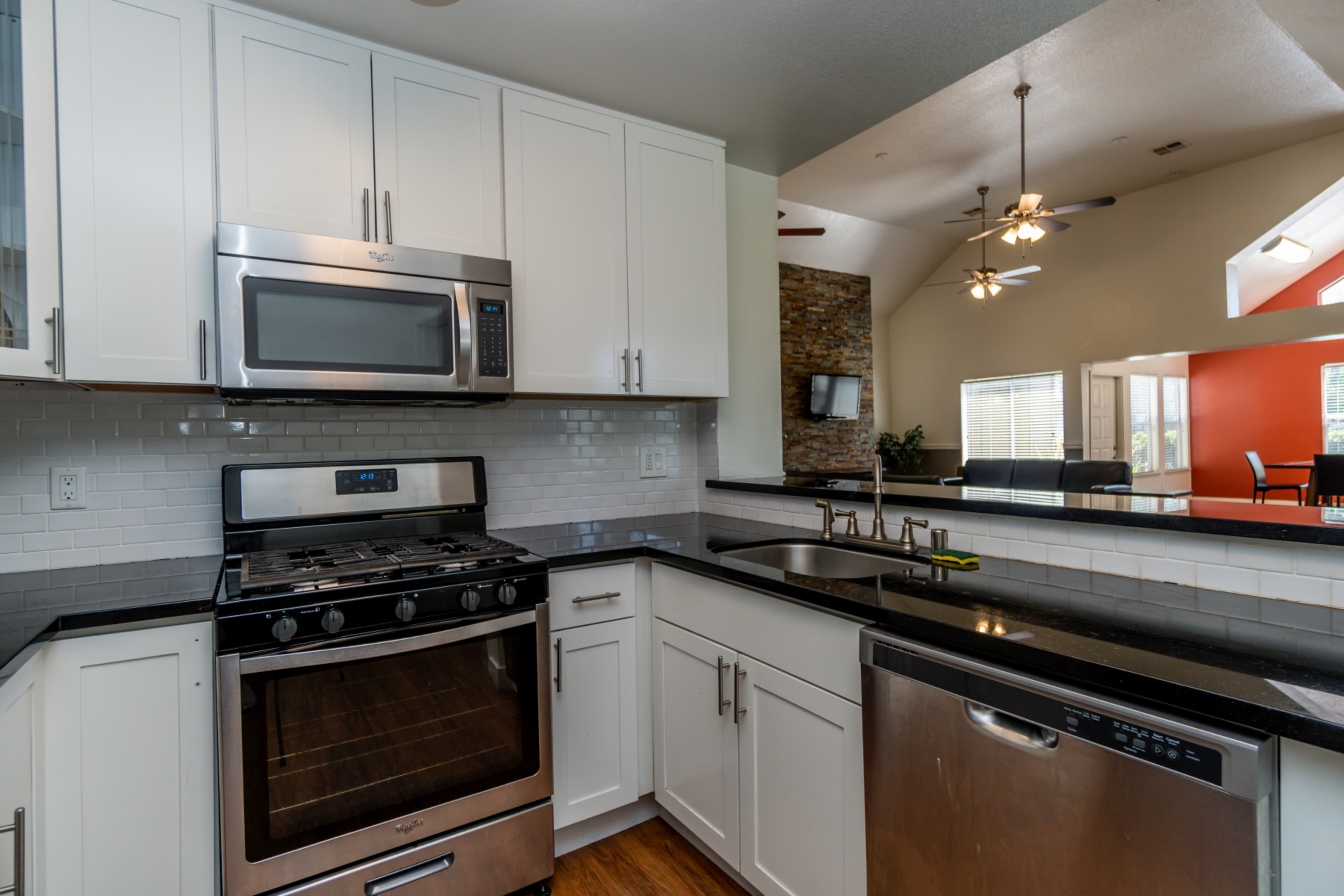 A modern kitchen featuring stainless steel appliances, white cabinetry, and a black countertop.