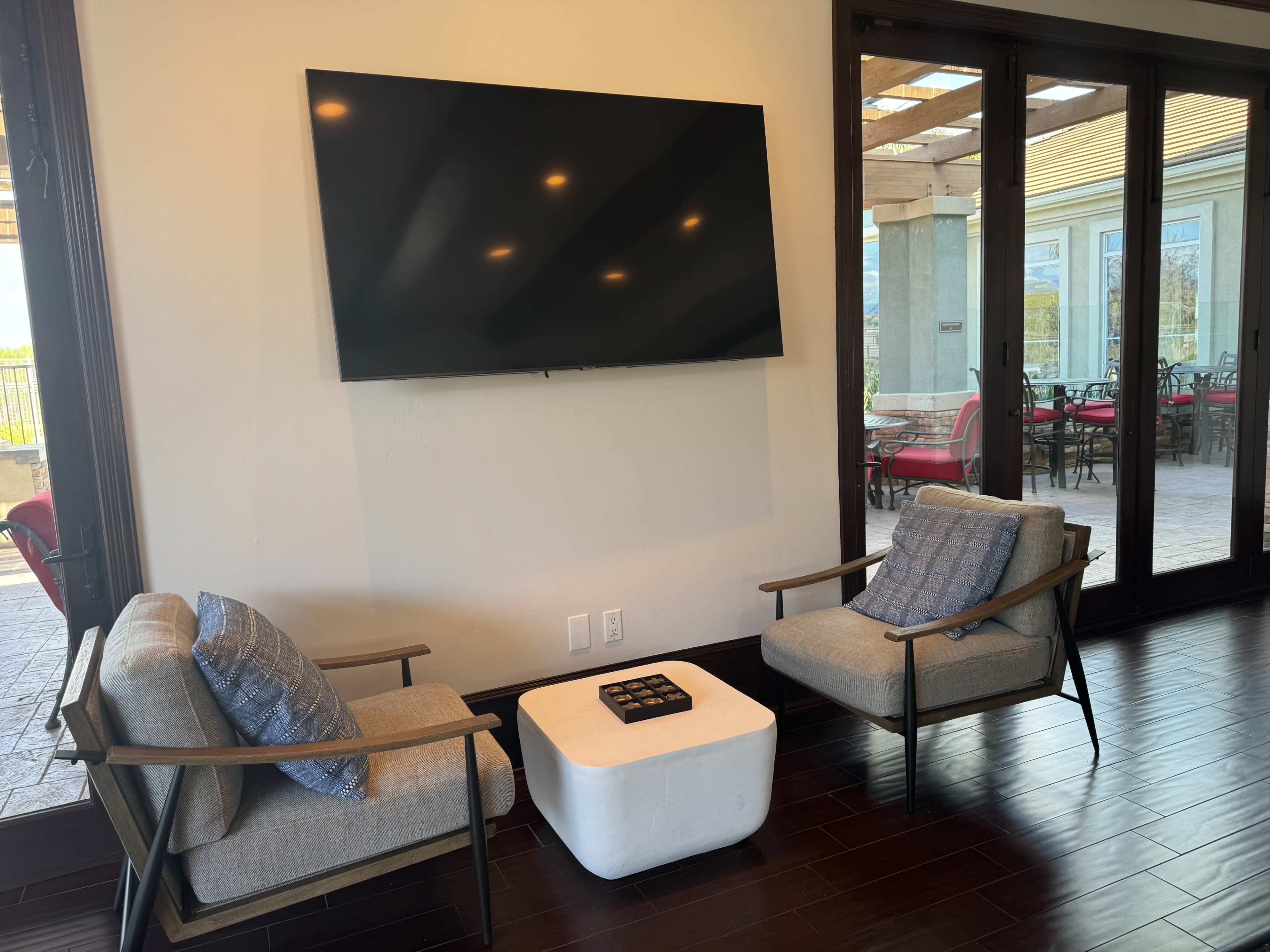 A modern living area features two armchairs facing a wall-mounted television, with a small white table positioned in between.