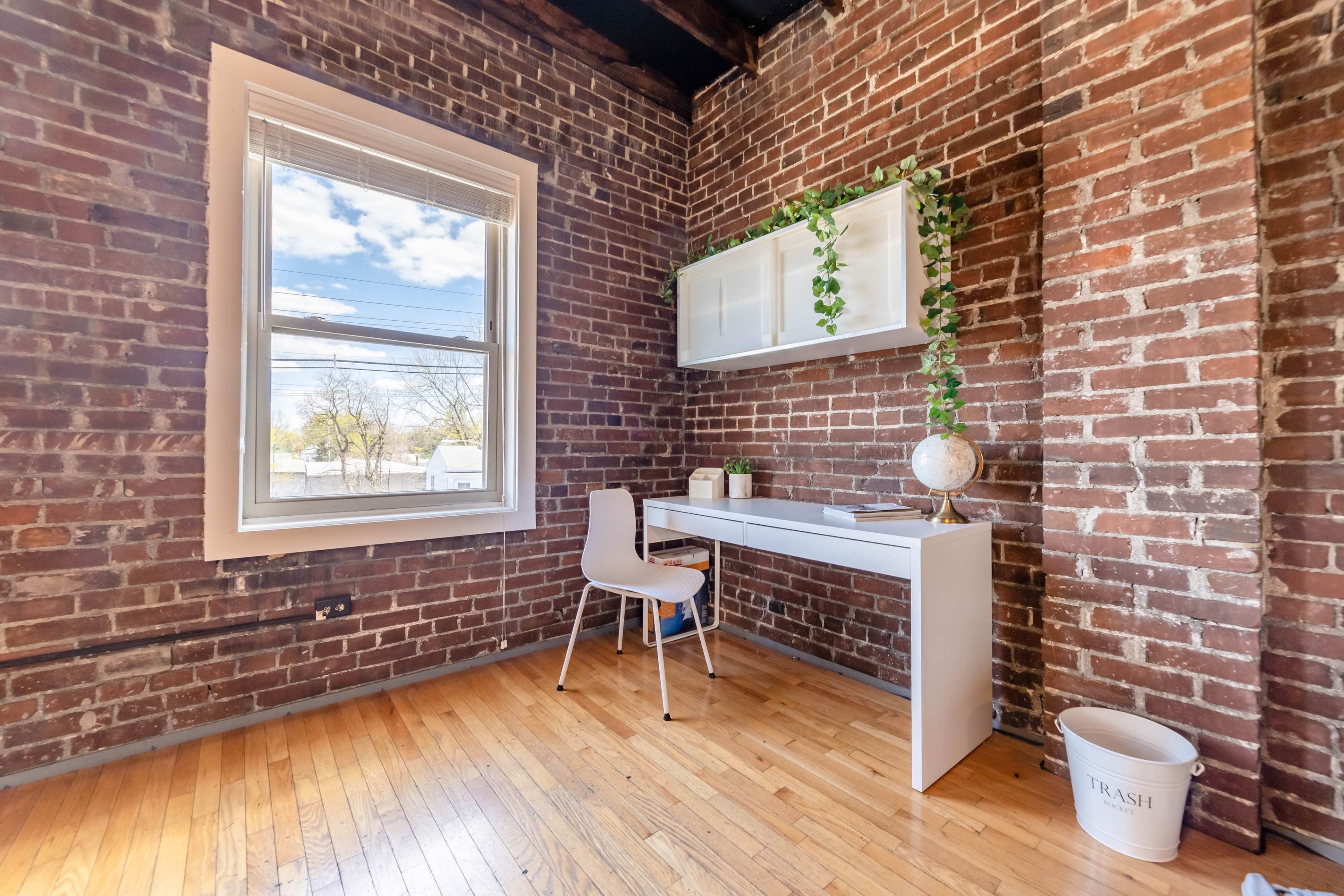 A small workspace featuring a white desk and chair against a brick wall, with a plant and decorative globe on the desk.