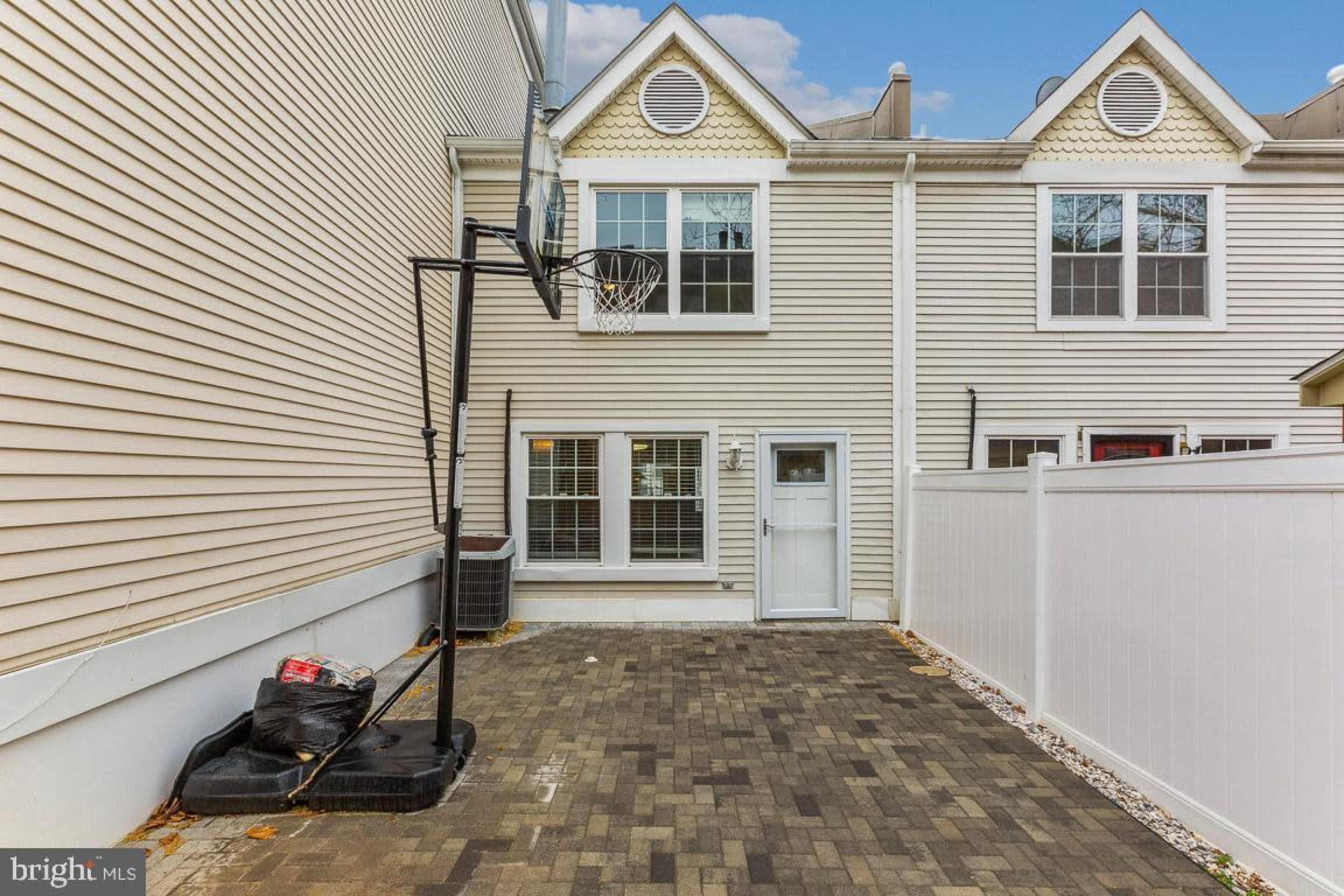 The image shows a backyard with a basketball hoop, a paved surface, and a white fence surrounding the area.