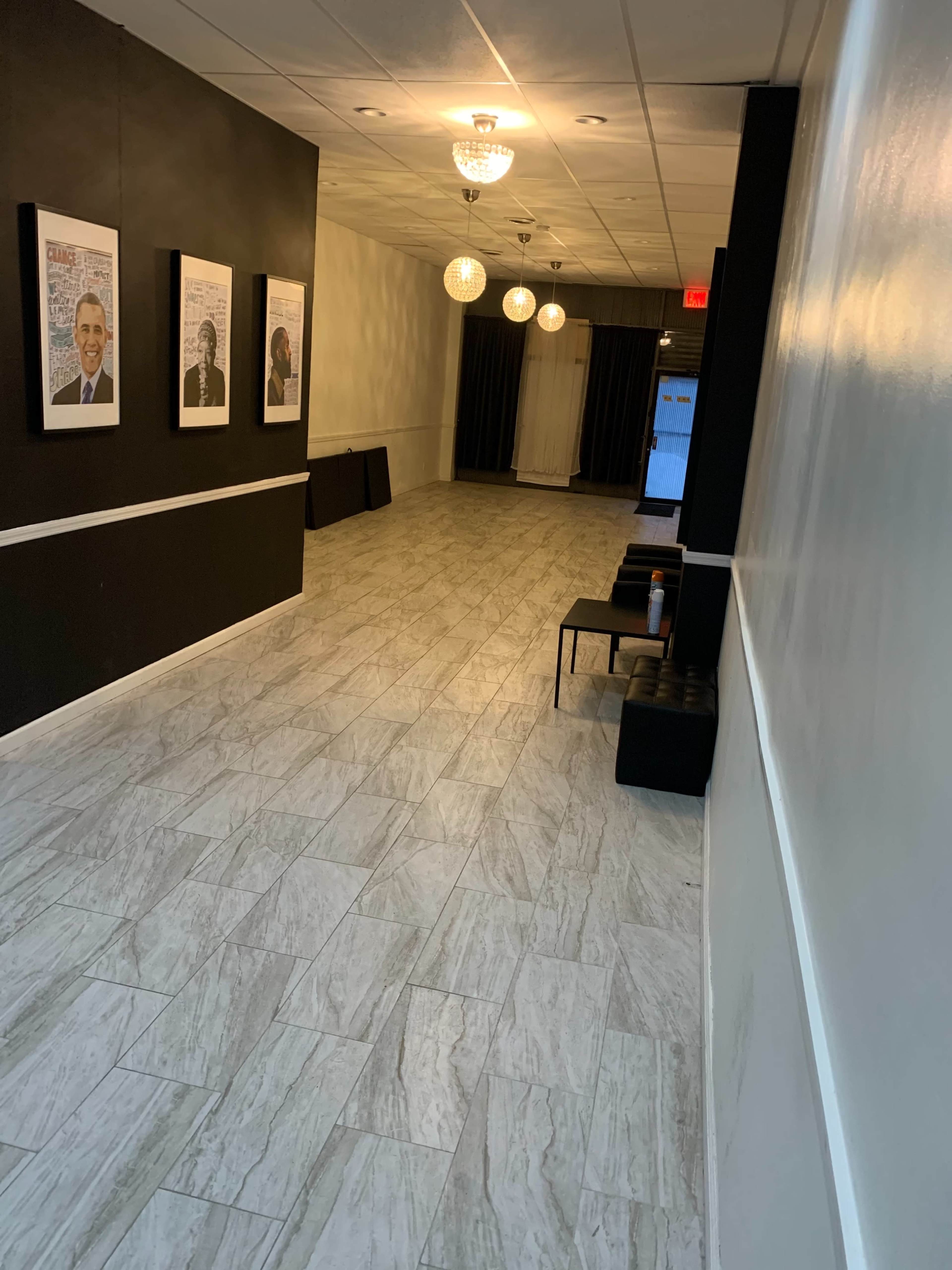 A long hallway with framed portraits on the left wall, a black curtain at the end, and a few light fixtures hanging from the ceiling.