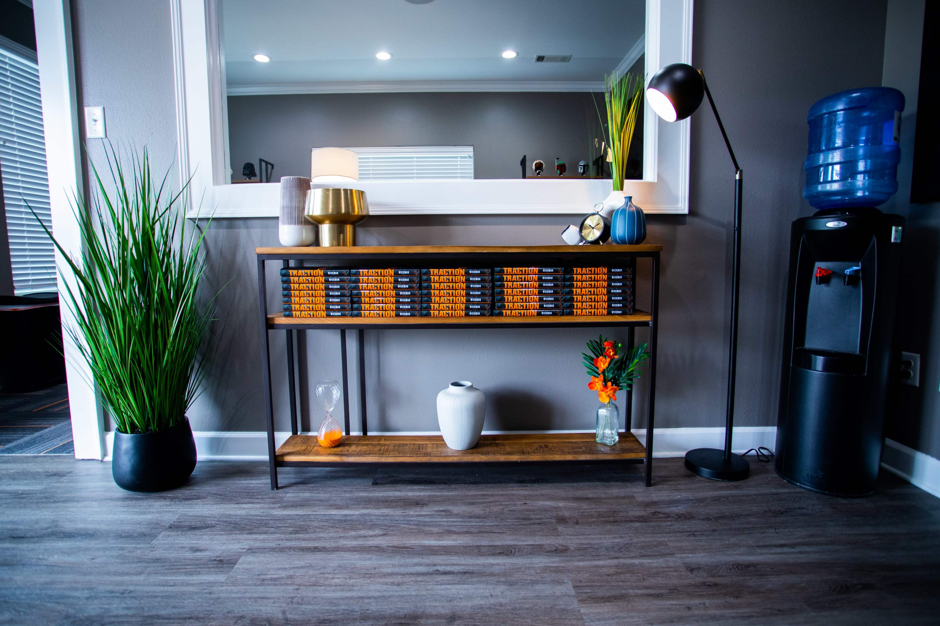 A wooden console table with decorative items and plants is positioned against a gray wall, beside a water cooler.