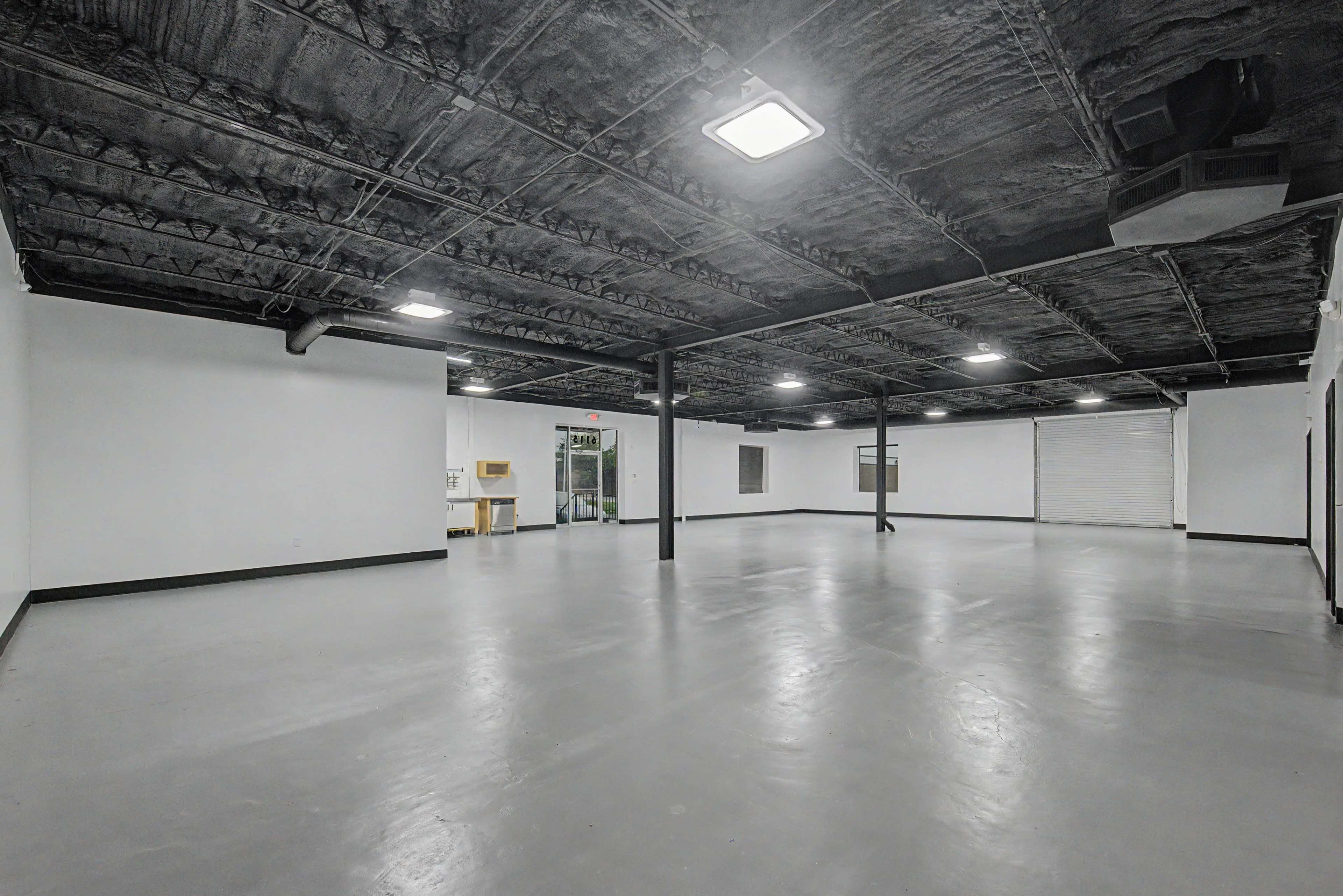 The image shows a large, empty commercial space with a concrete floor and exposed beams on the ceiling.