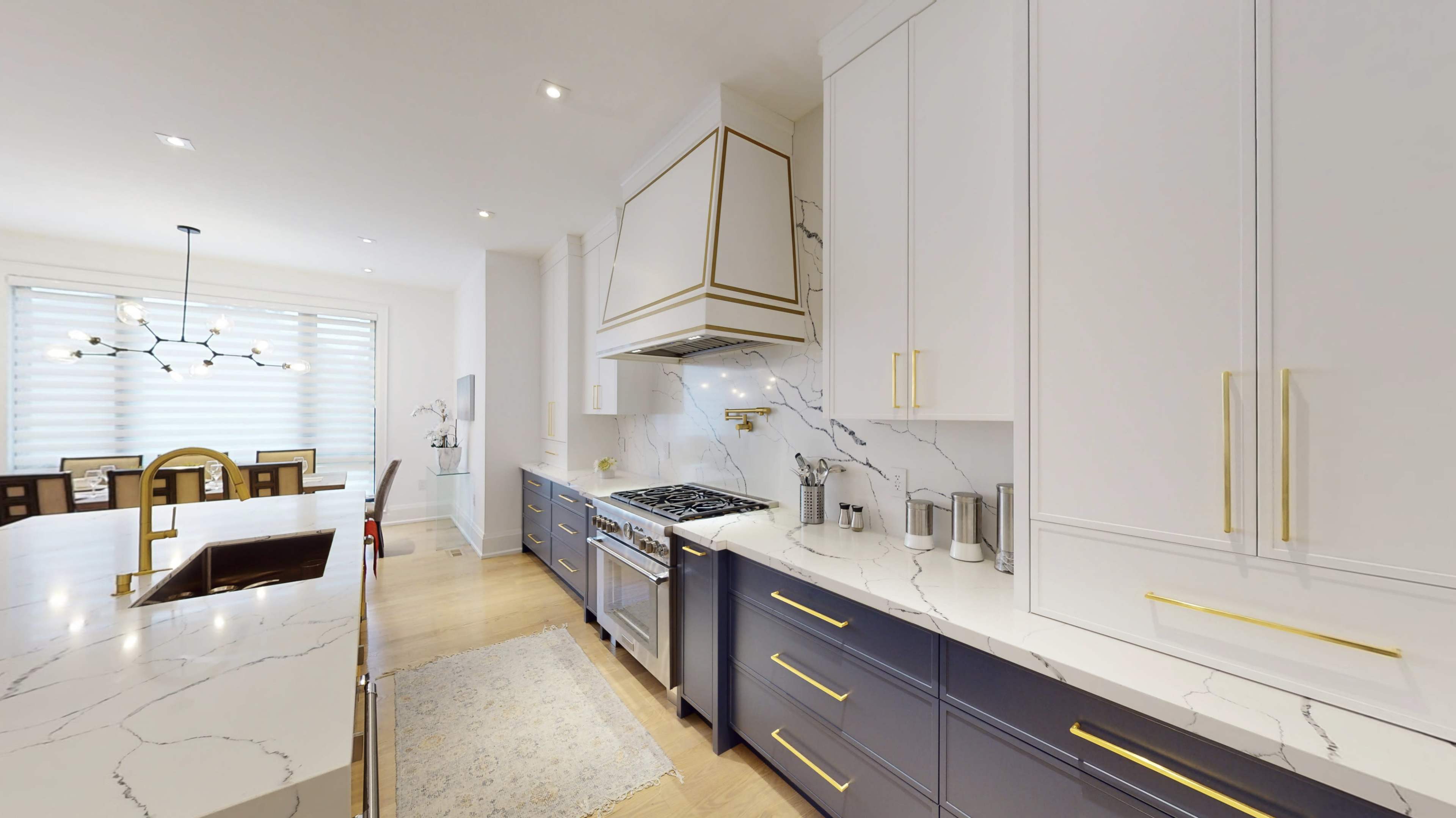 The kitchen features white and navy cabinetry with gold hardware, a marble countertop, and a large island with a gas stove and overhead range hood.