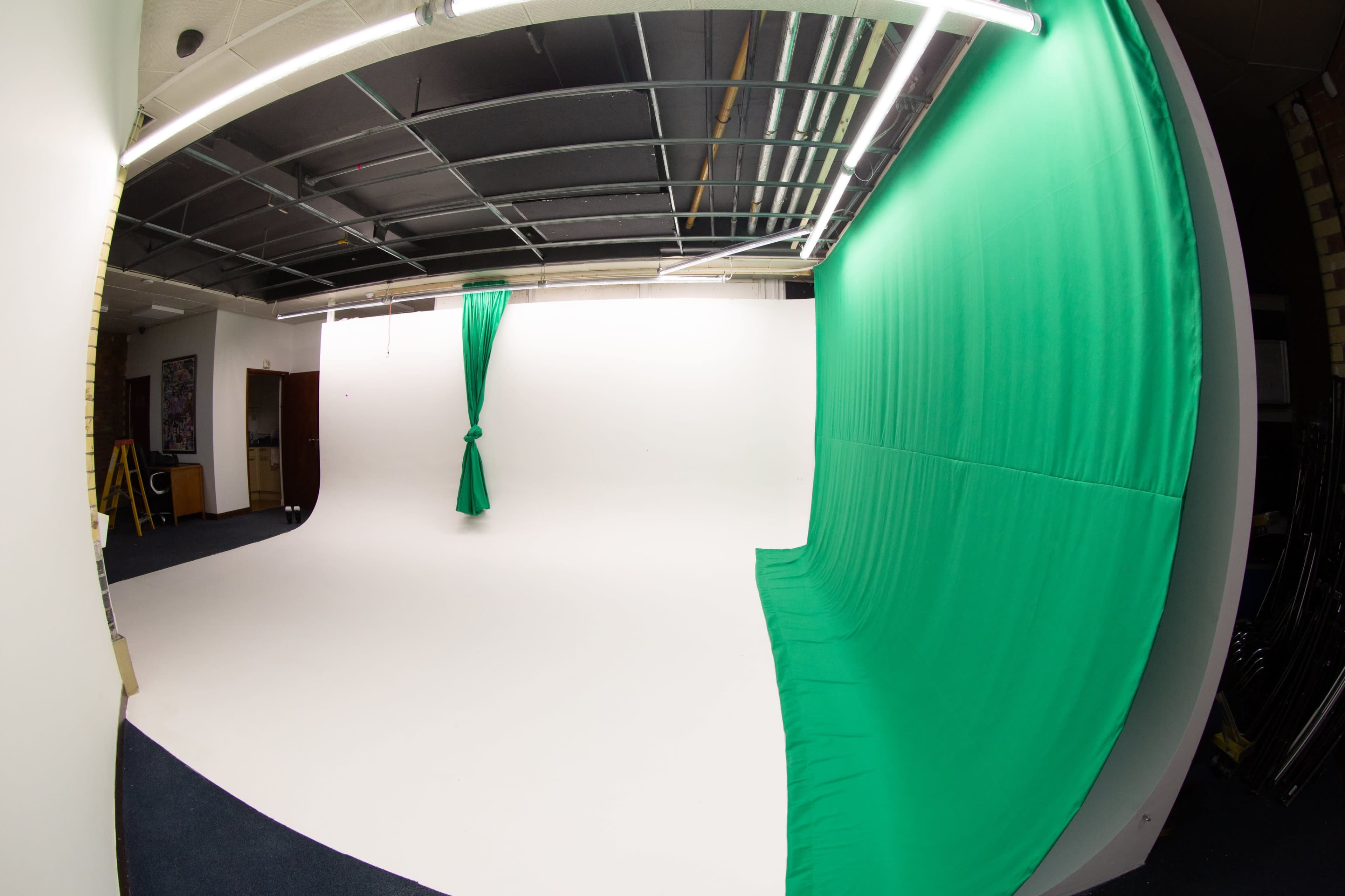 A photography studio featuring a white backdrop and a green curtain draped on one side.