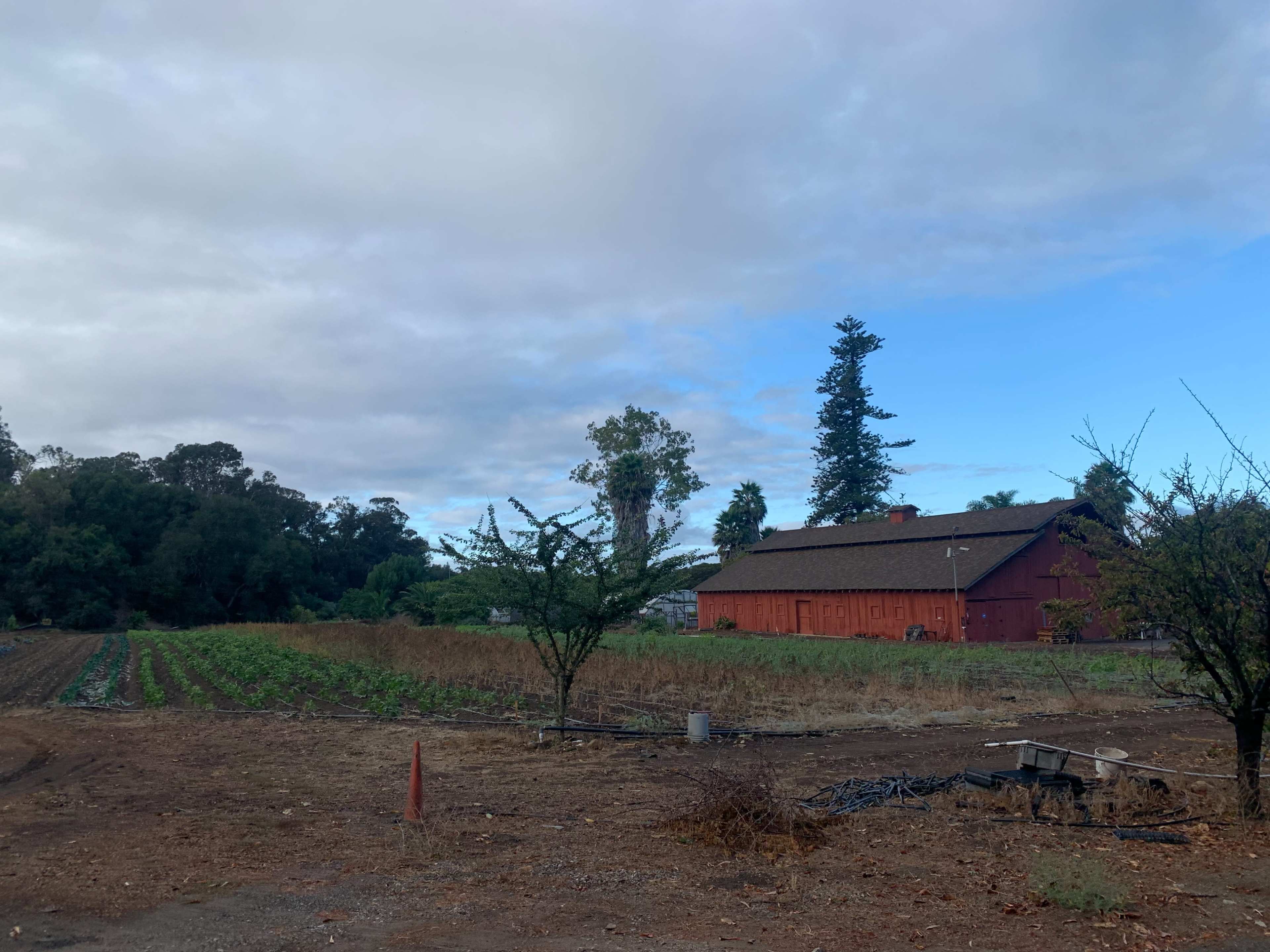 A red barn sits beside rows of crop fields under a partly cloudy sky.