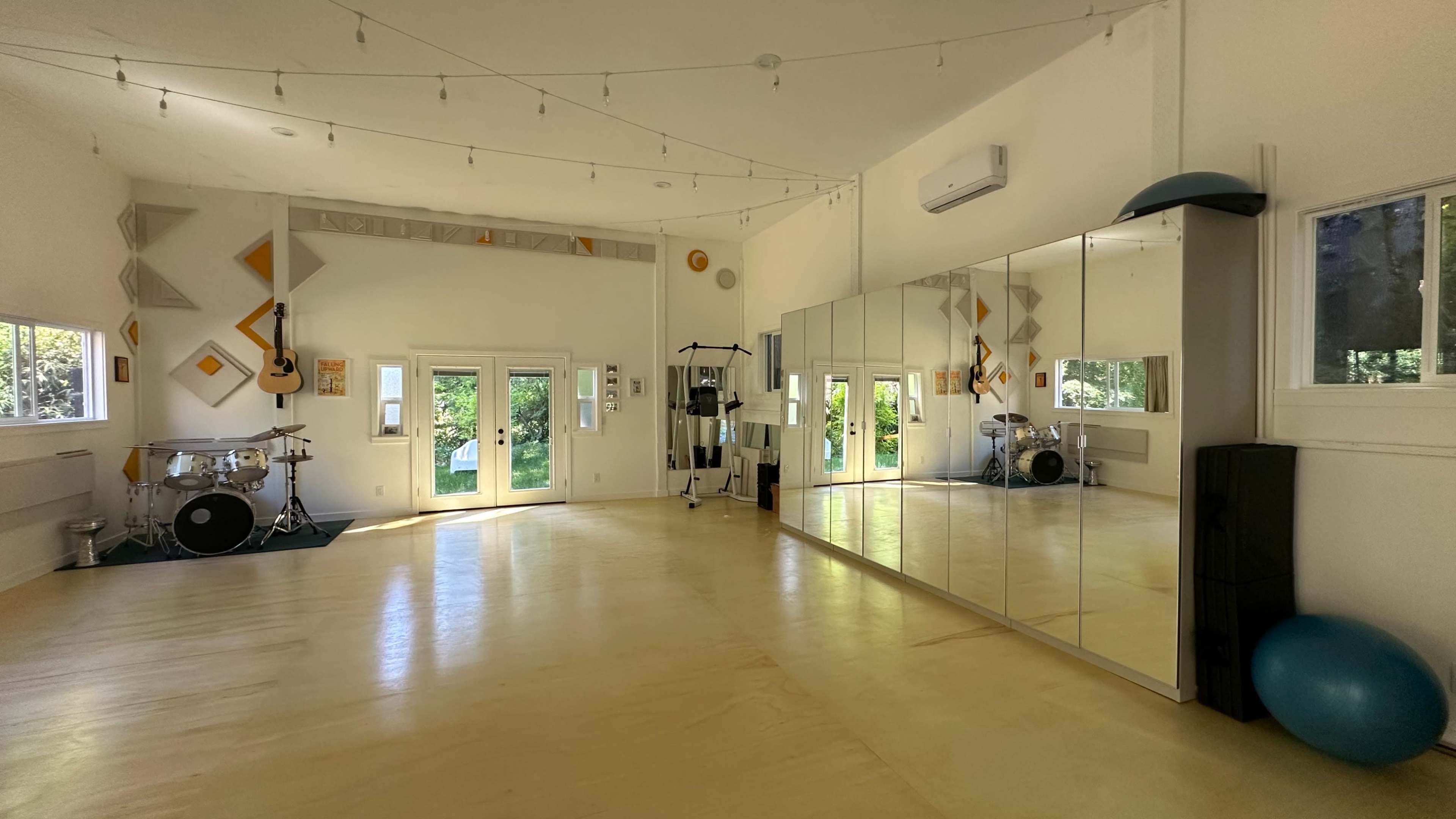 The image shows a spacious dance or practice studio with large mirrors, wooden floors, and natural light coming through multiple windows.