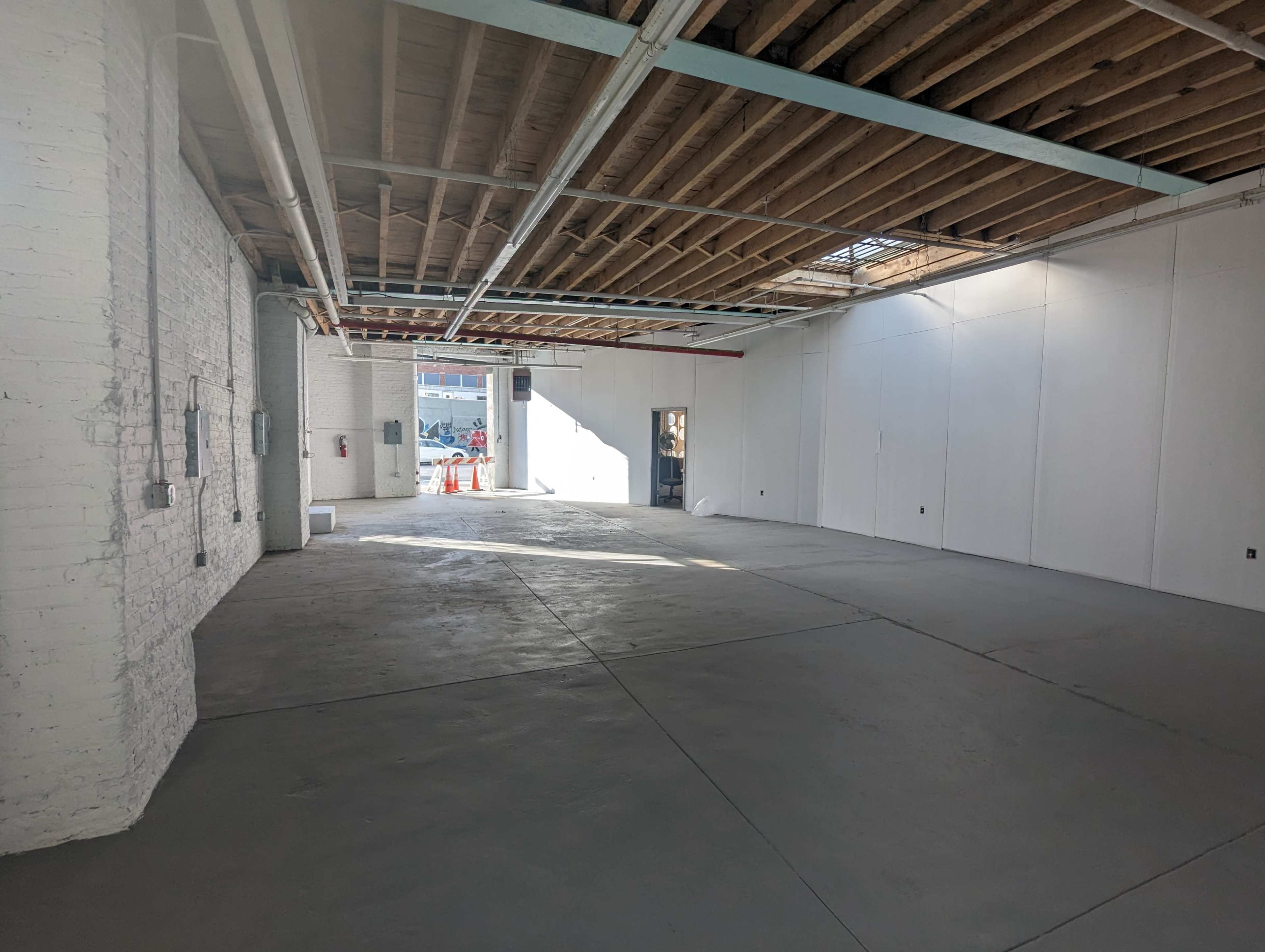 The image shows a spacious, empty warehouse interior with concrete flooring and exposed wooden beams overhead.