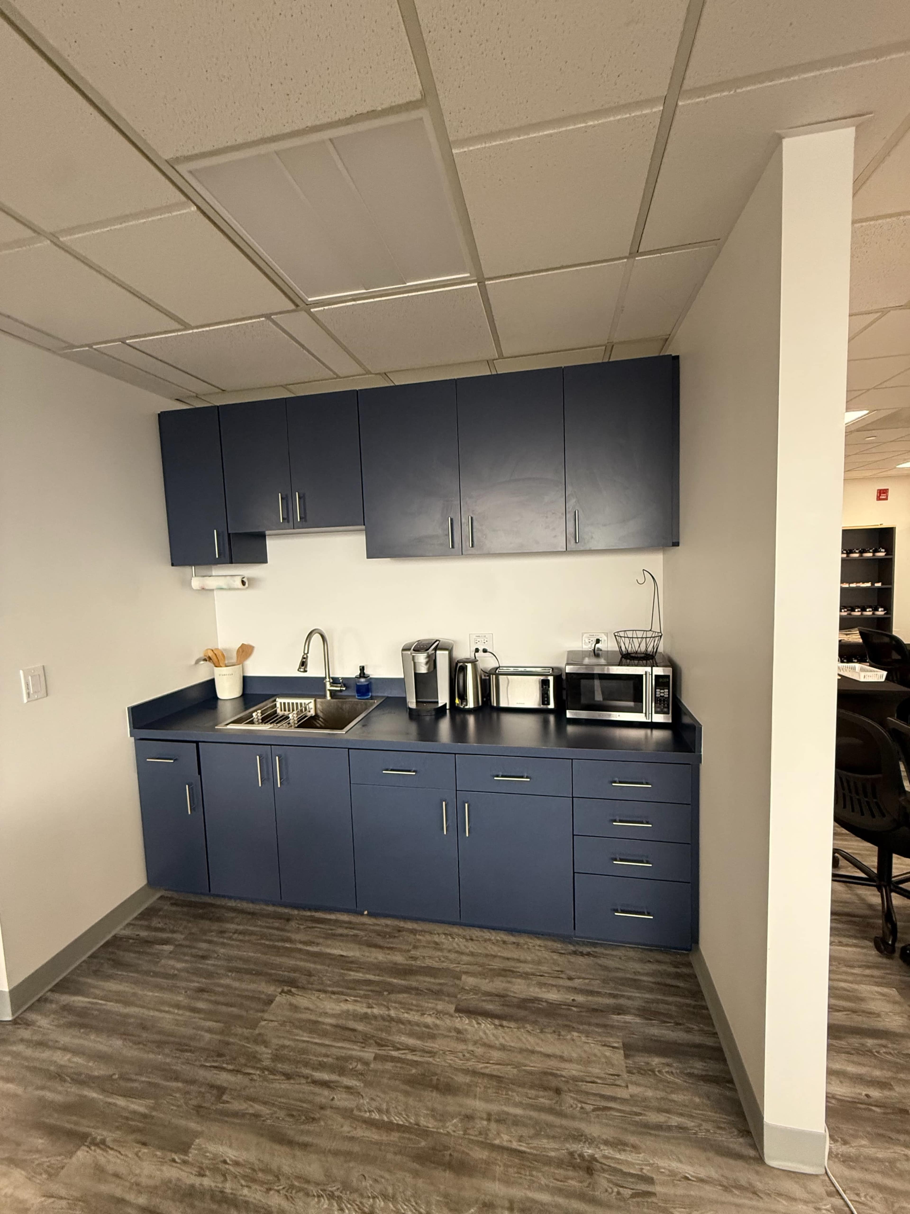The image shows a modern kitchen area featuring dark blue cabinets, a stainless steel sink, a coffee maker, a microwave, and various kitchen utensils.
