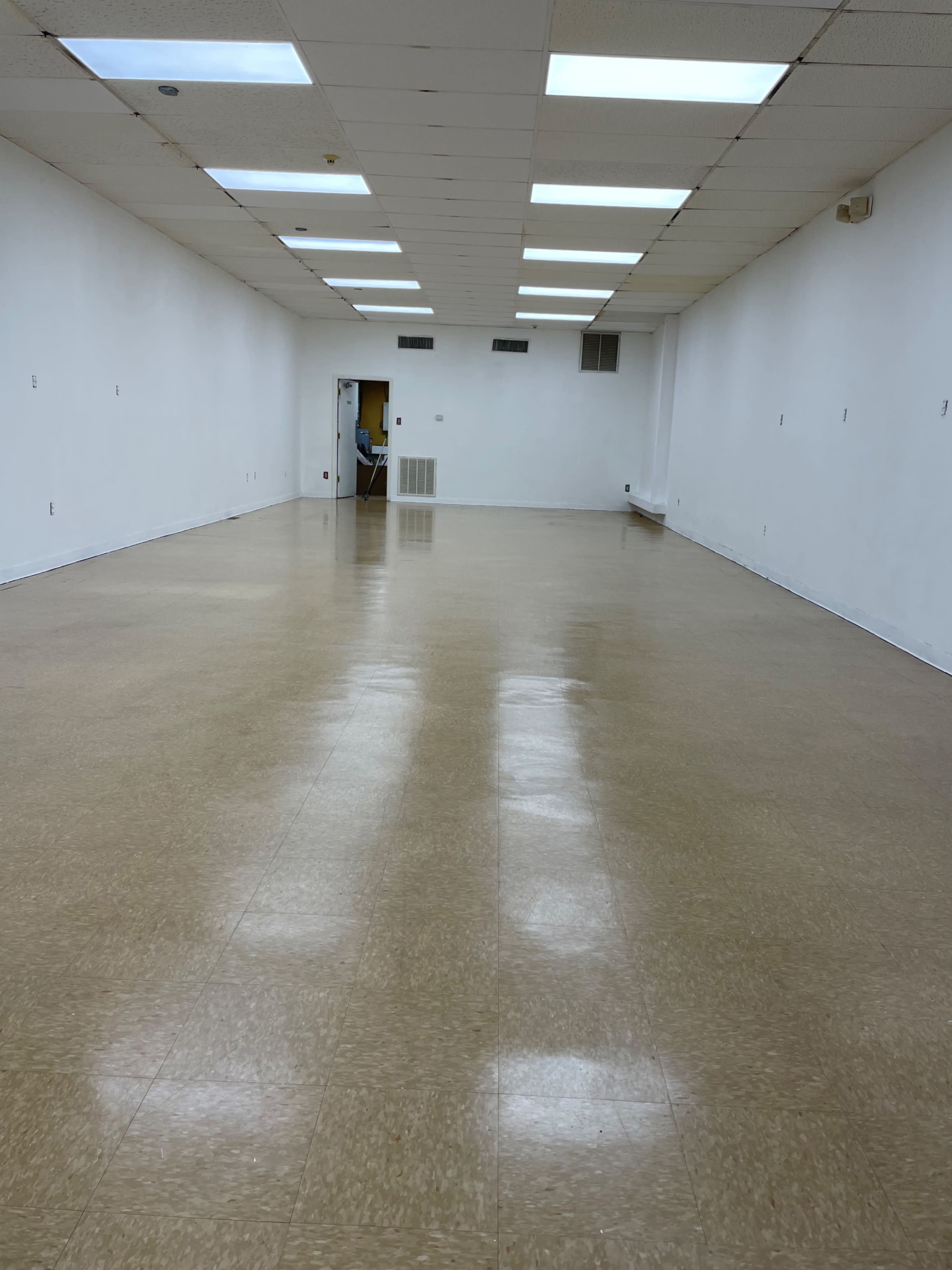 A large, empty room with a polished floor and white walls, illuminated by overhead lights.