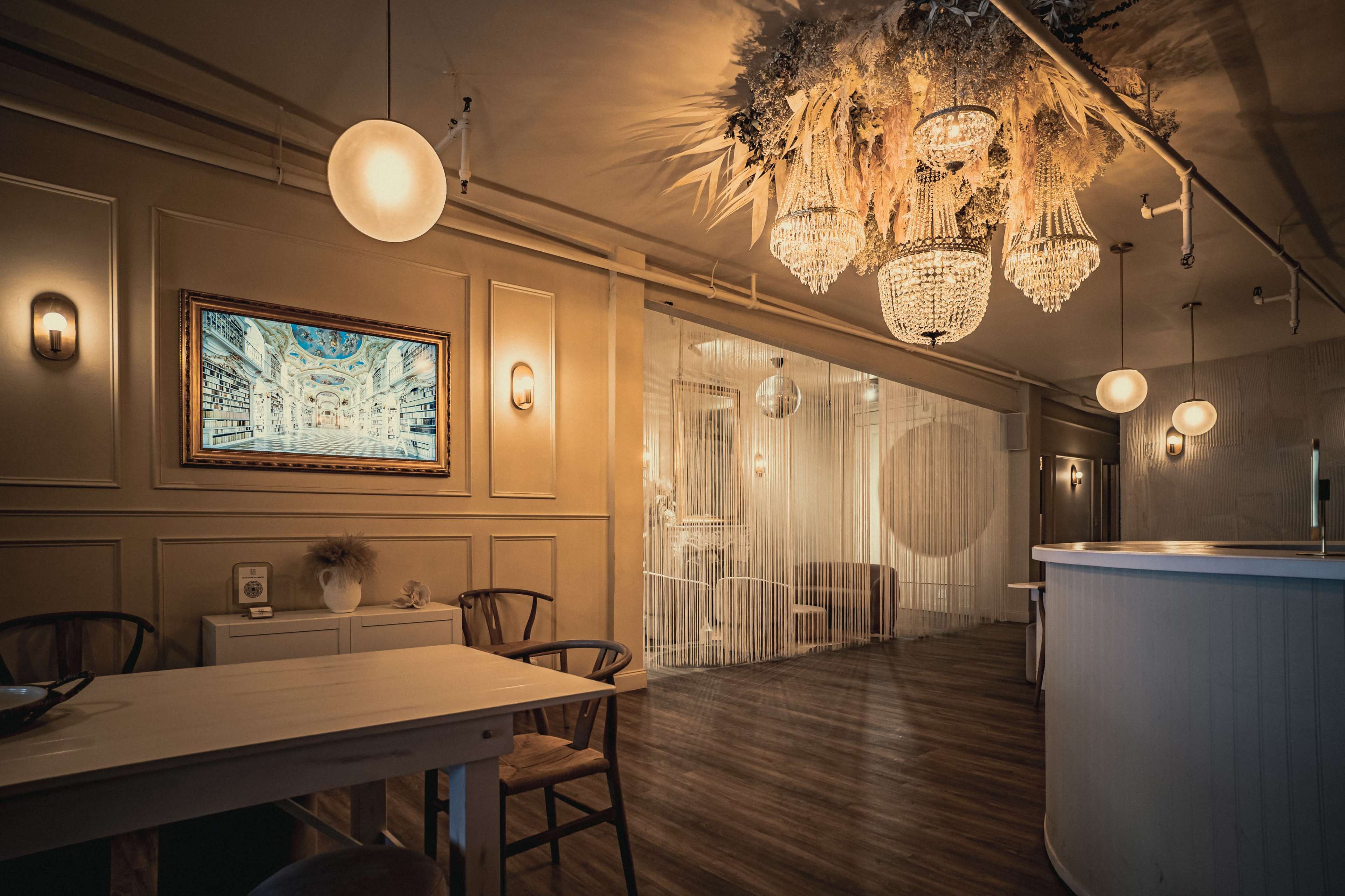 A well-lit interior space featuring a blend of elegant chandeliers, framed artwork, and a cozy dining area.
