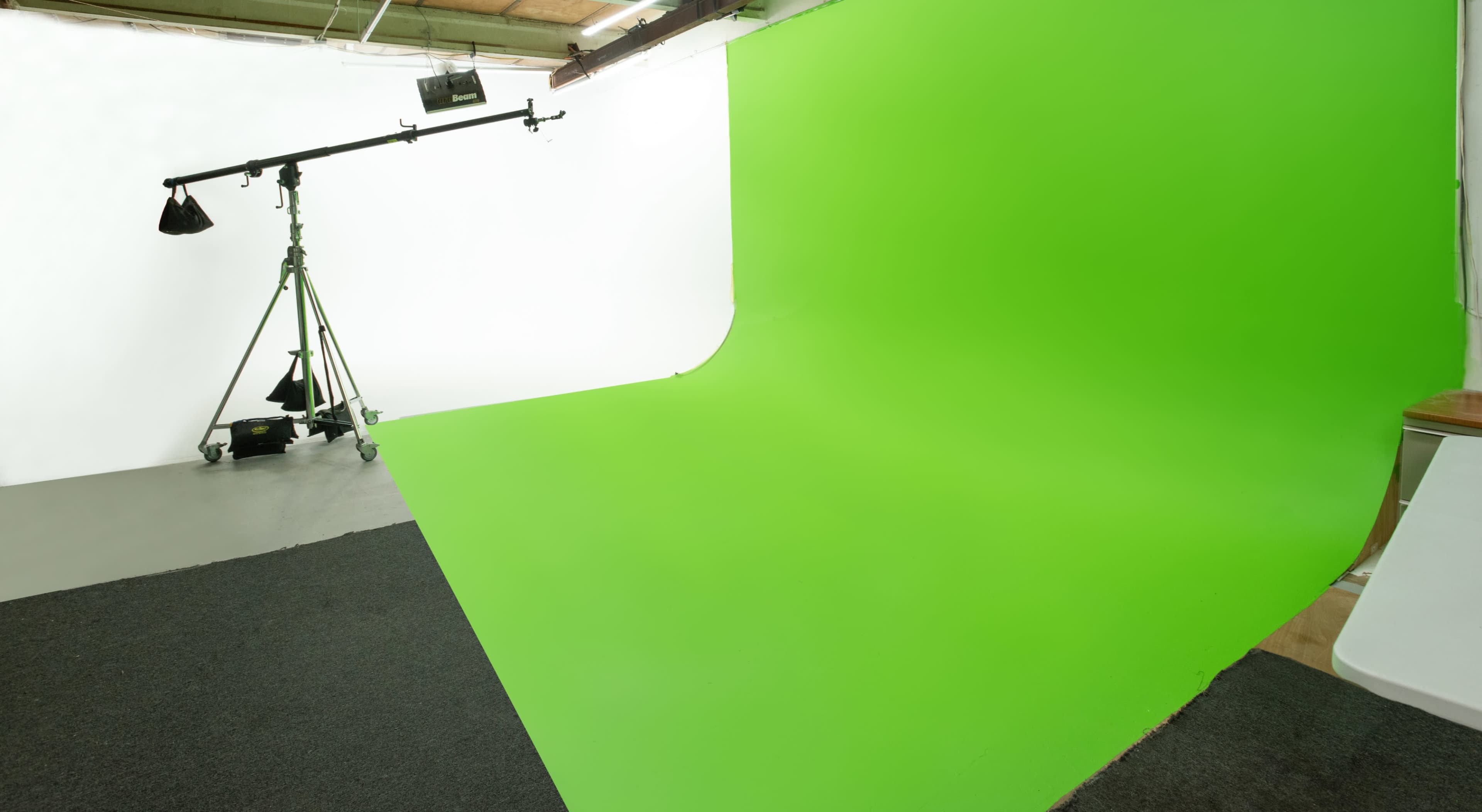 The image shows a photography studio with a green screen backdrop, a white wall, and a lighting rig on a stand.