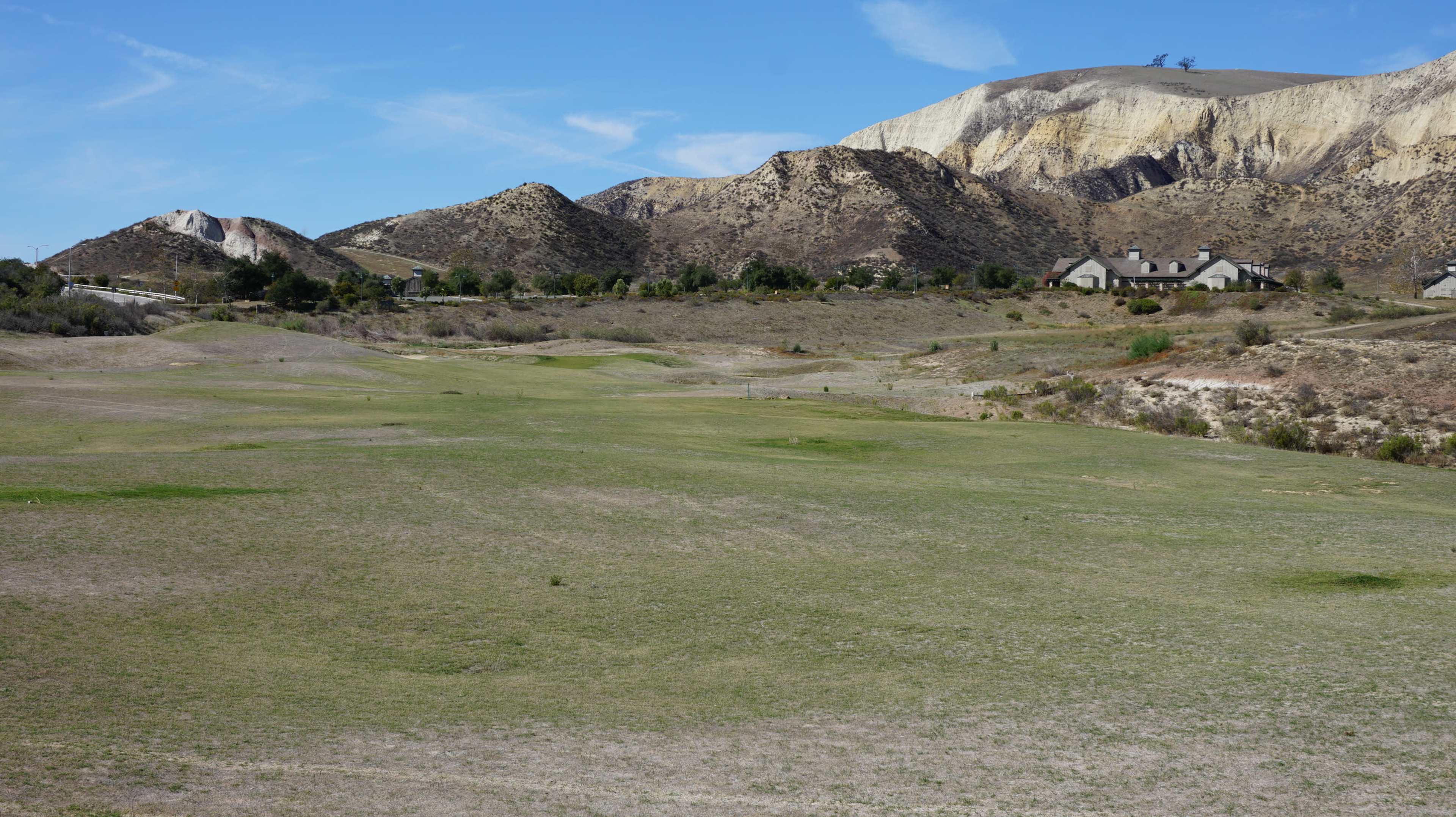 A wide view of a dry, grassy landscape with low hills and a few houses in the background.